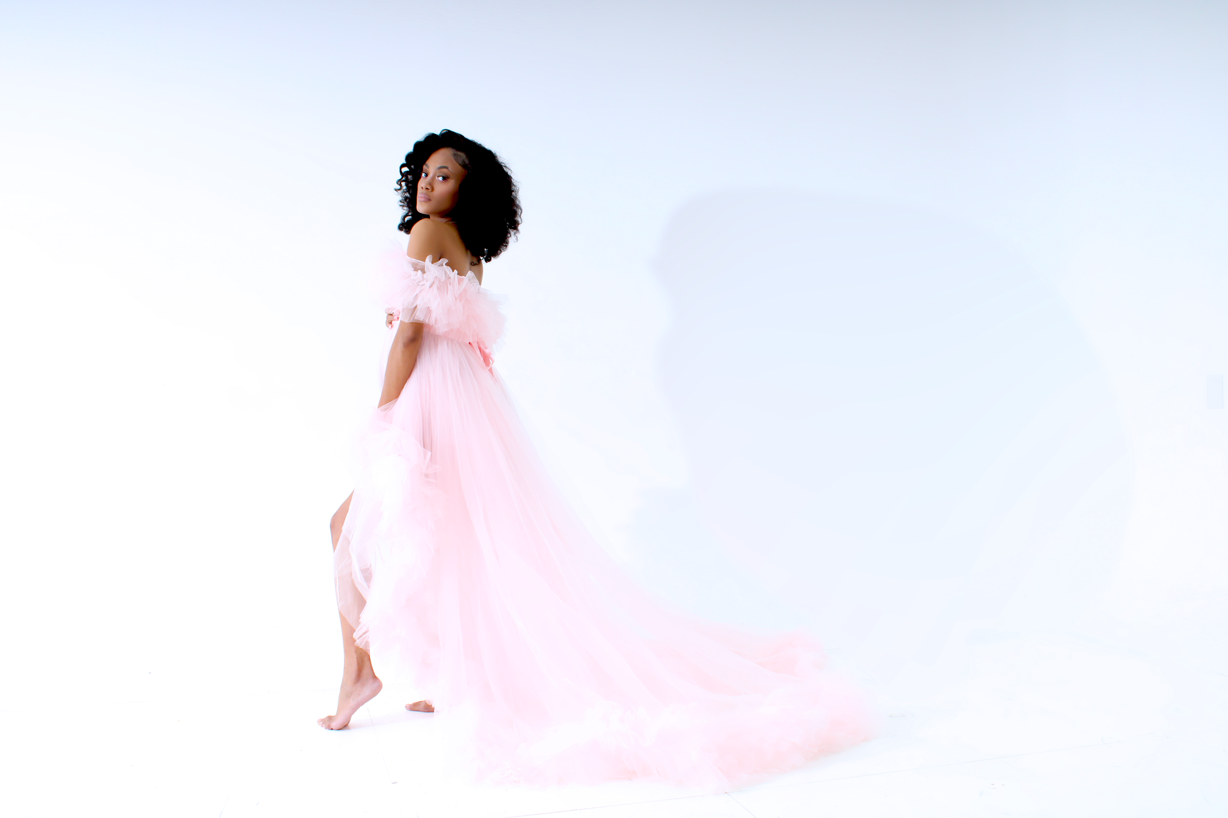 Woman in a flowing pink gown standing barefoot against a white background.