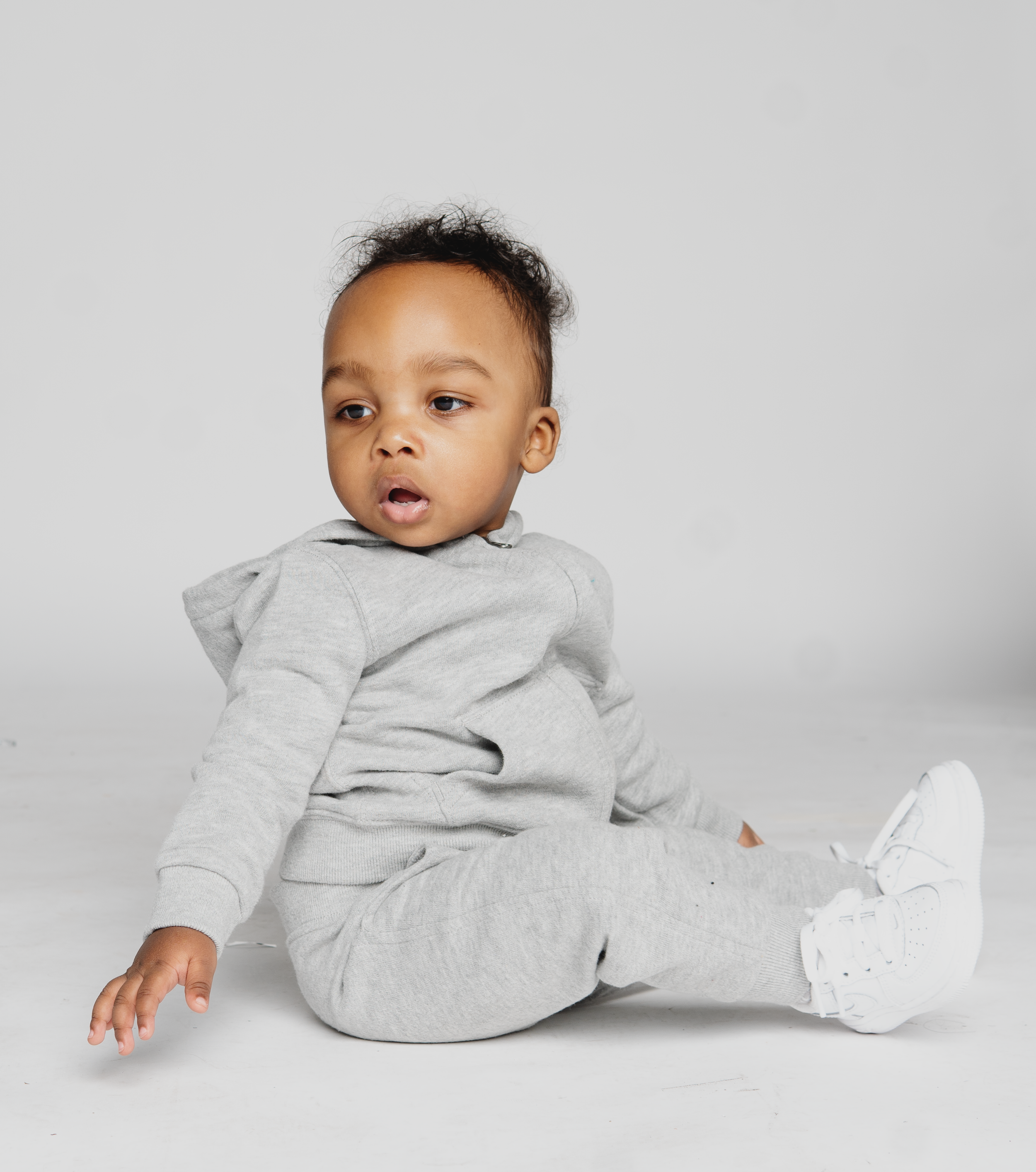 Baby in a gray tracksuit sitting on a white background.