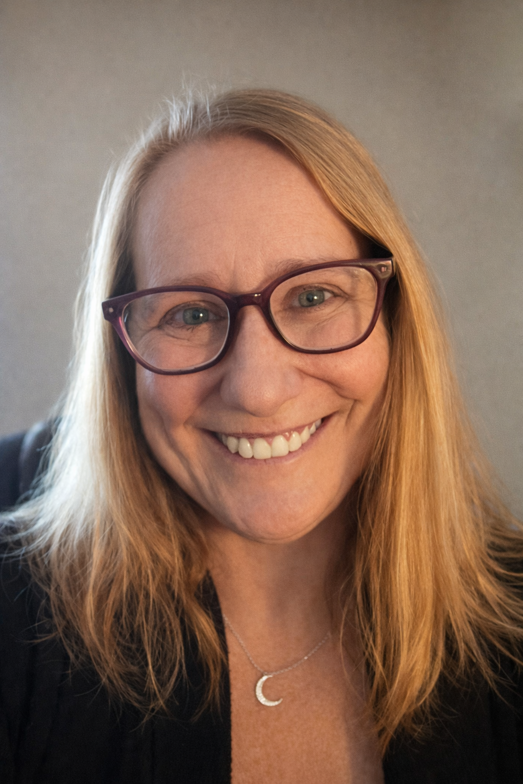 A woman with shoulder-length strawberry blonde hair and glasses smiling at the camera.