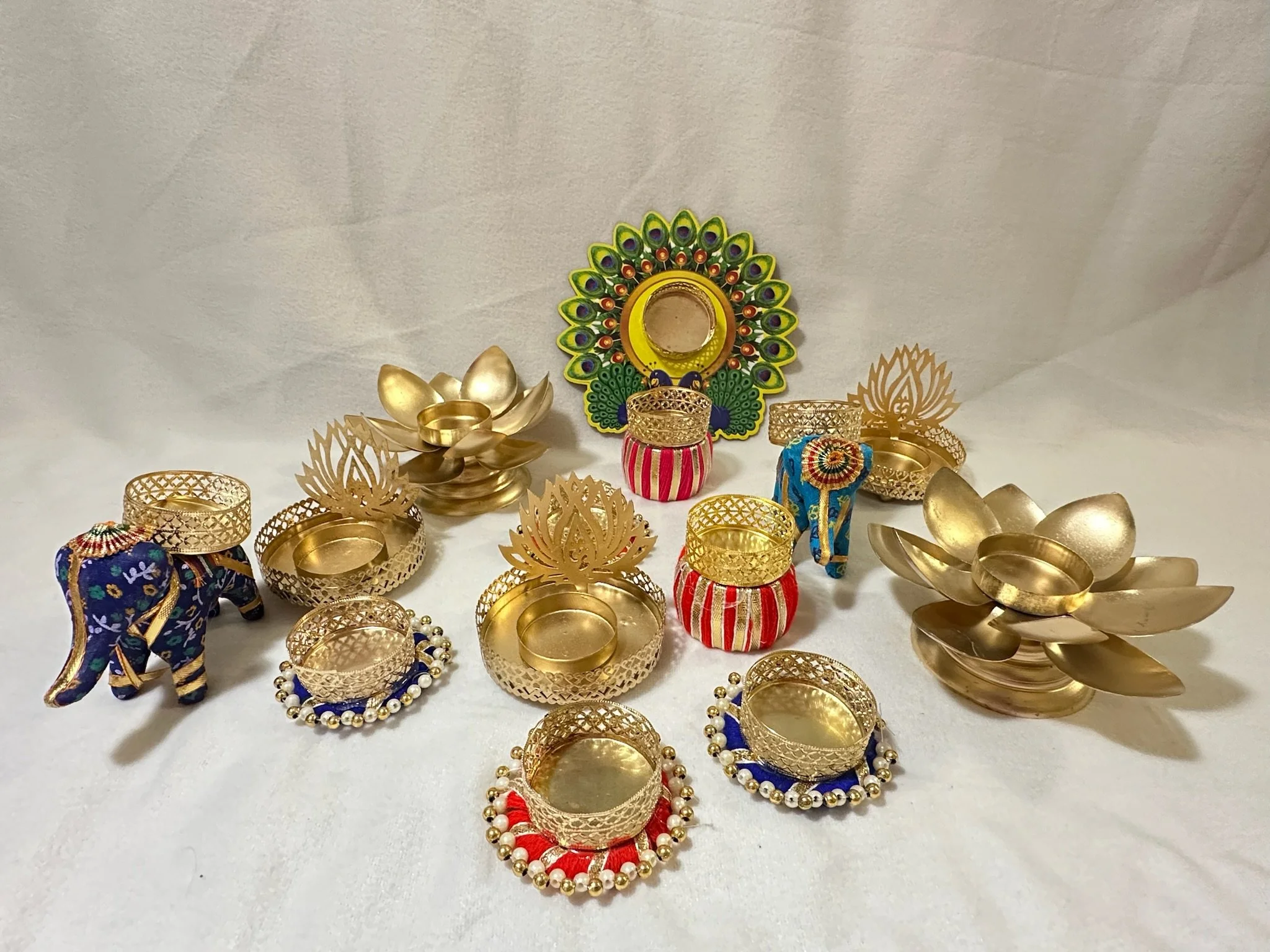 Decorative gold-colored items including lotus-shaped candle holders, ornate boxes, embroidered elephant, and a peacock feather design mirror