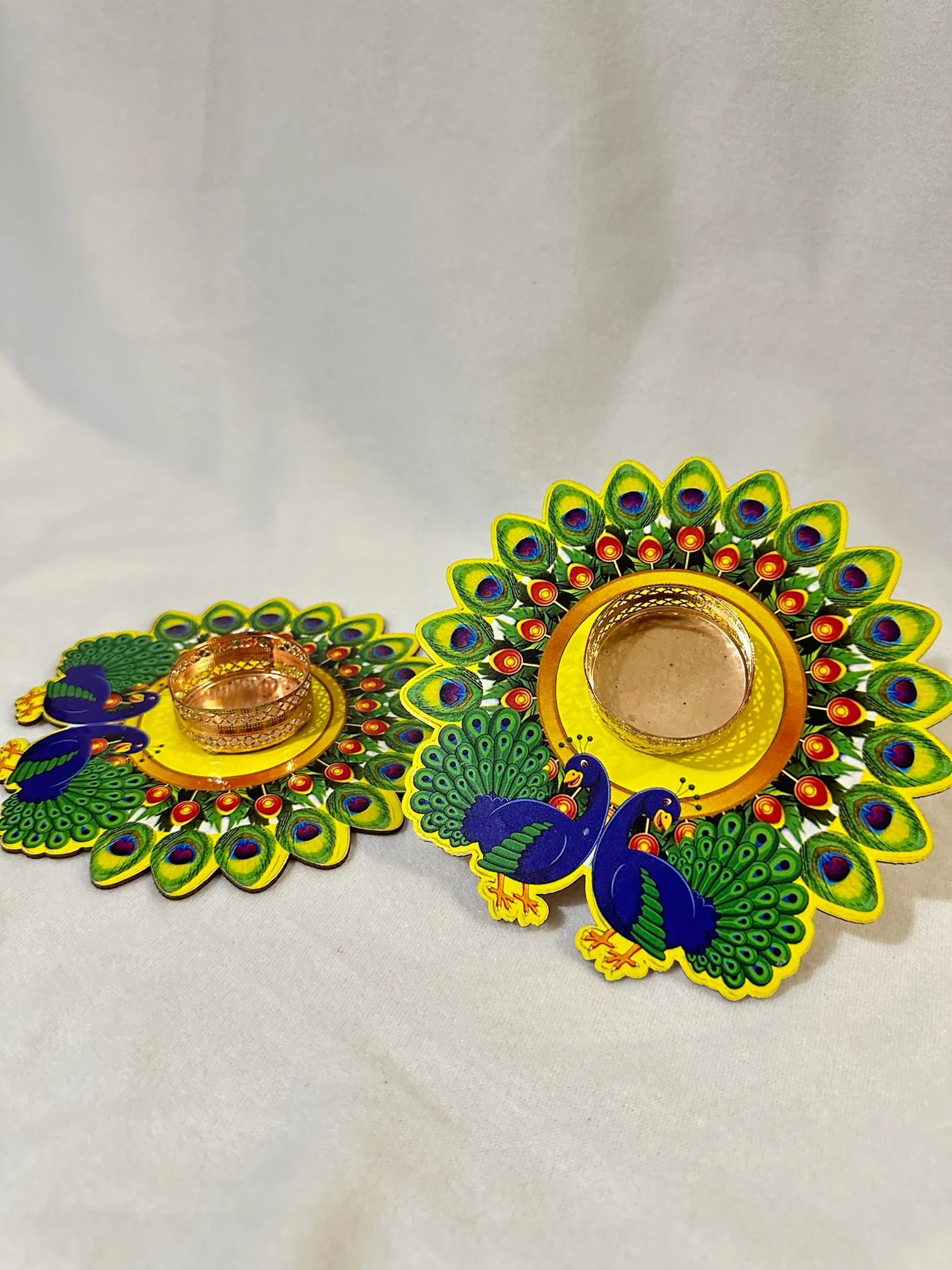Decorative peacock-shaped candle holders with small glass tealight holders, colorful peacock feather designs, on a white surface.