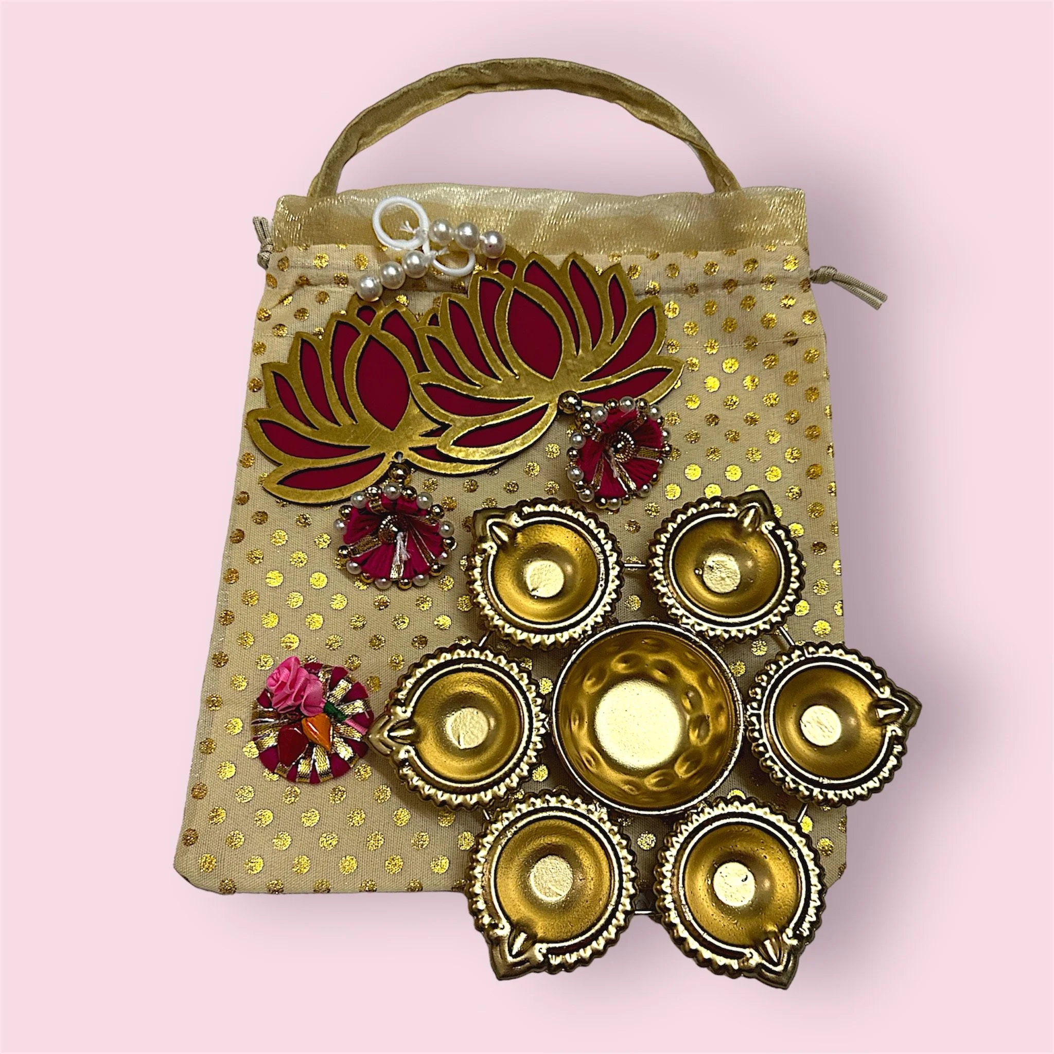 Collection of decorative jewelry and items on a golden and polka-dotted cloth bag, including a lotus flower-shaped brooch, hanging earrings, and small gold-colored bowls.