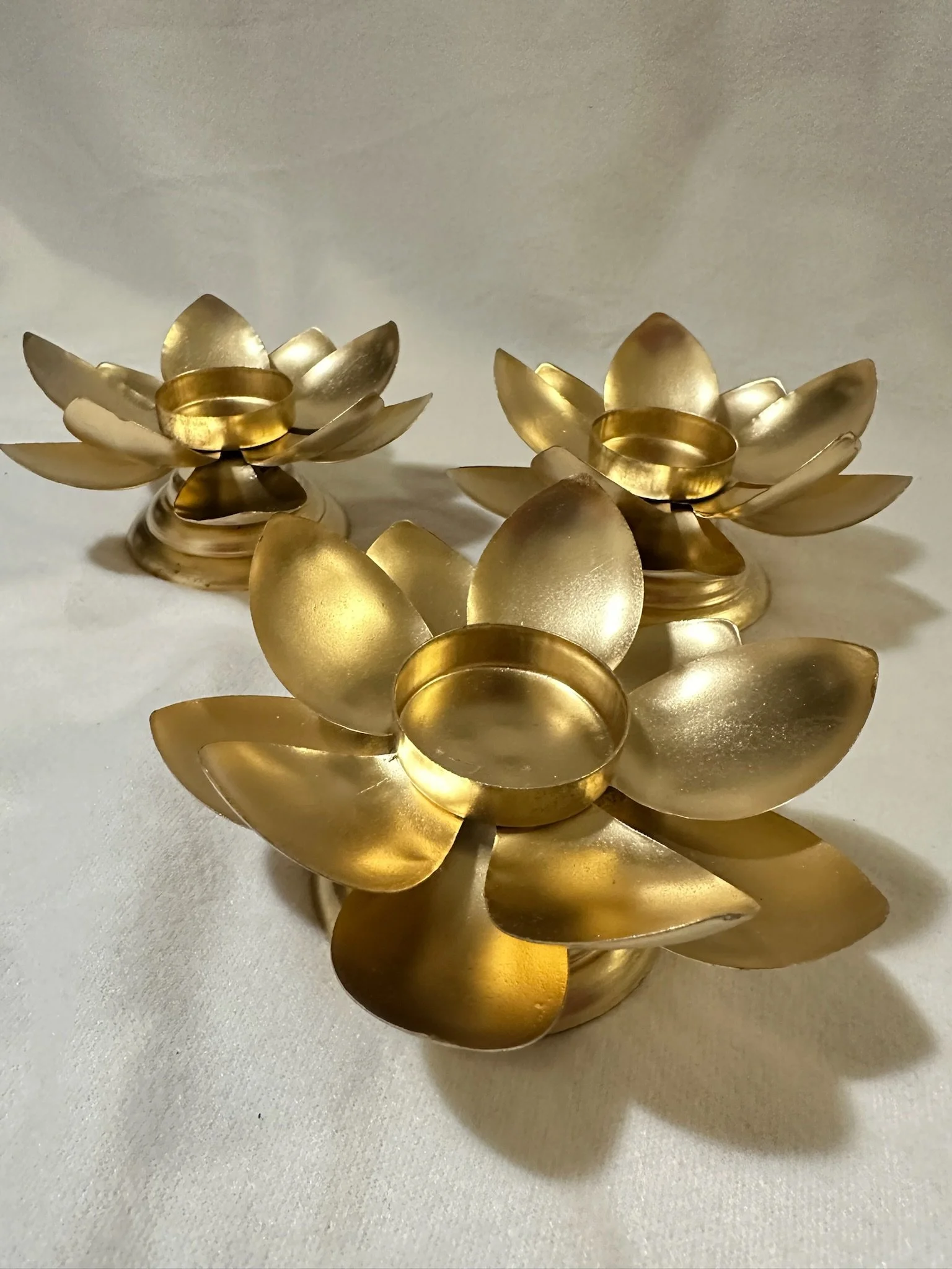 Three gold lotus-shaped candle holders with petal-like extensions are placed on a white surface.