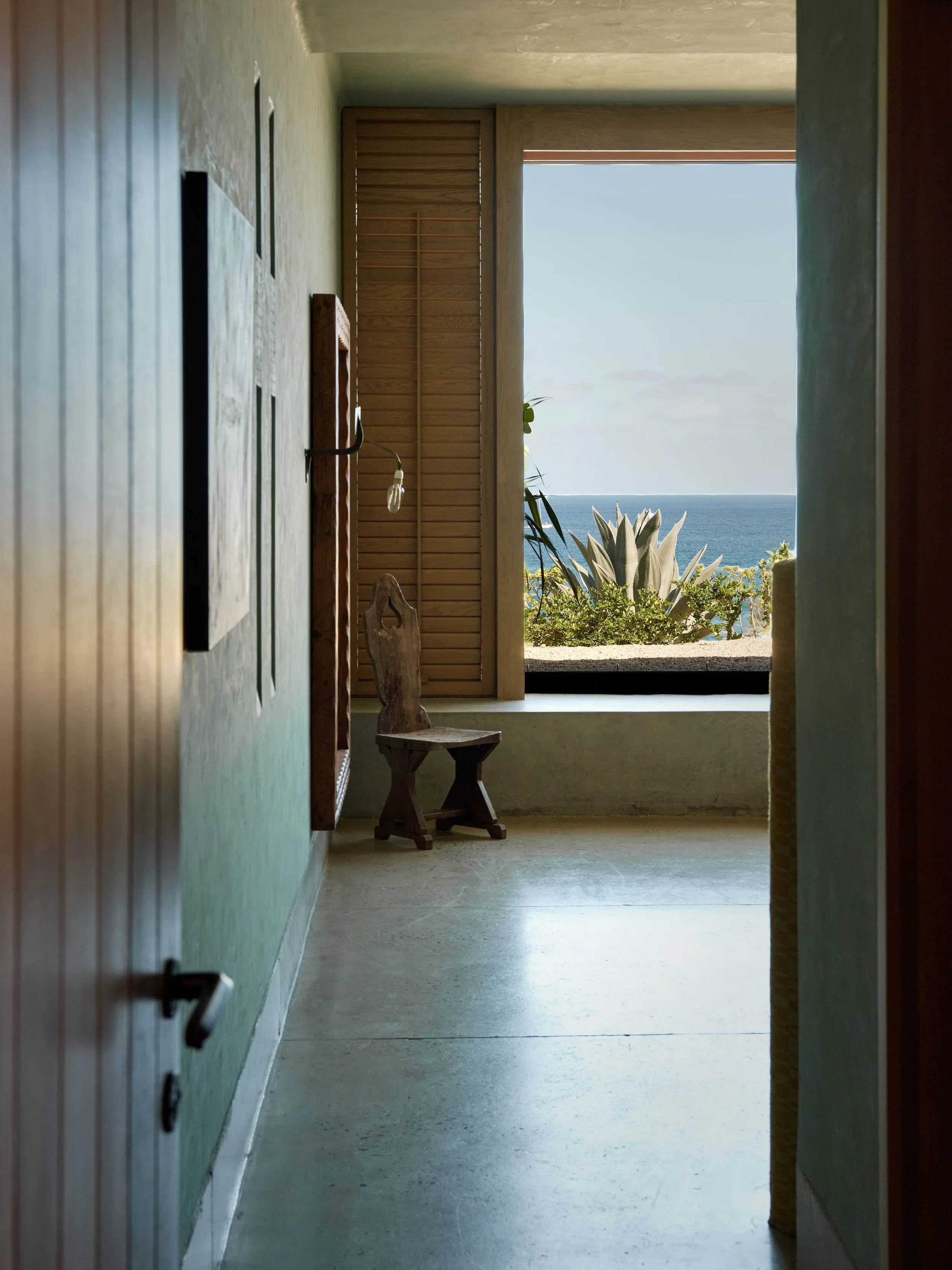A hallway with a window showing outdoor plants and the ocean view.
