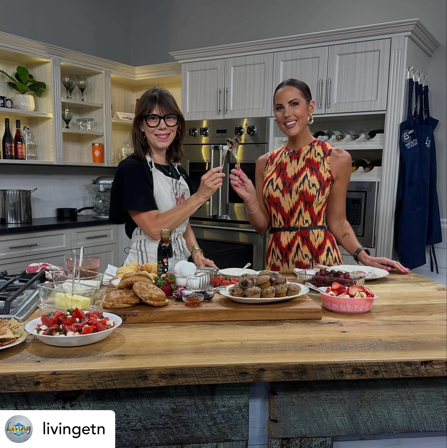 Two women in a kitchen preparing food and desserts, with various pastries, strawberries, and other ingredients on the counter.
