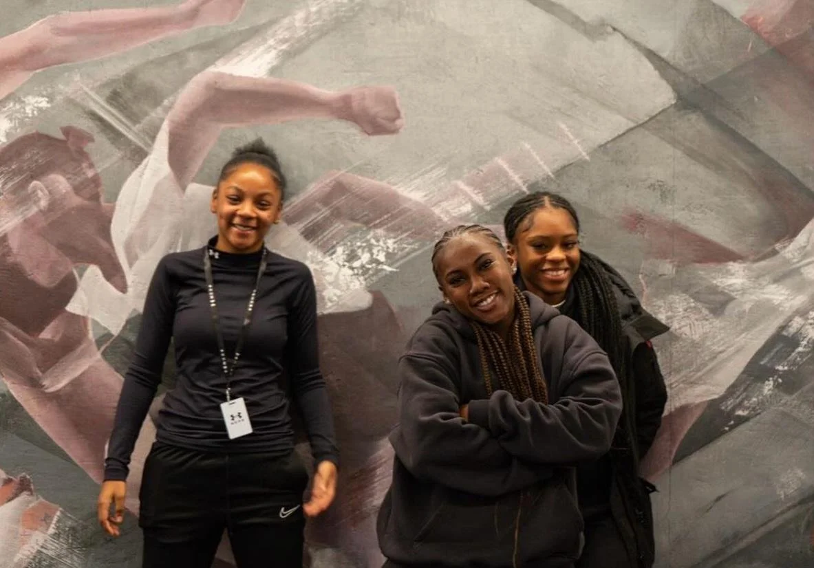 Three women standing in front of a large abstract painting, smiling at the camera.
