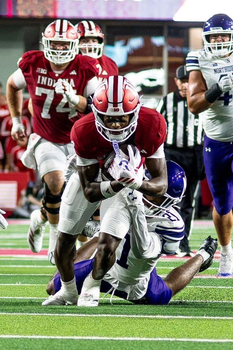 Indiana ball carrier fighting through a Northwestern tackle at night.