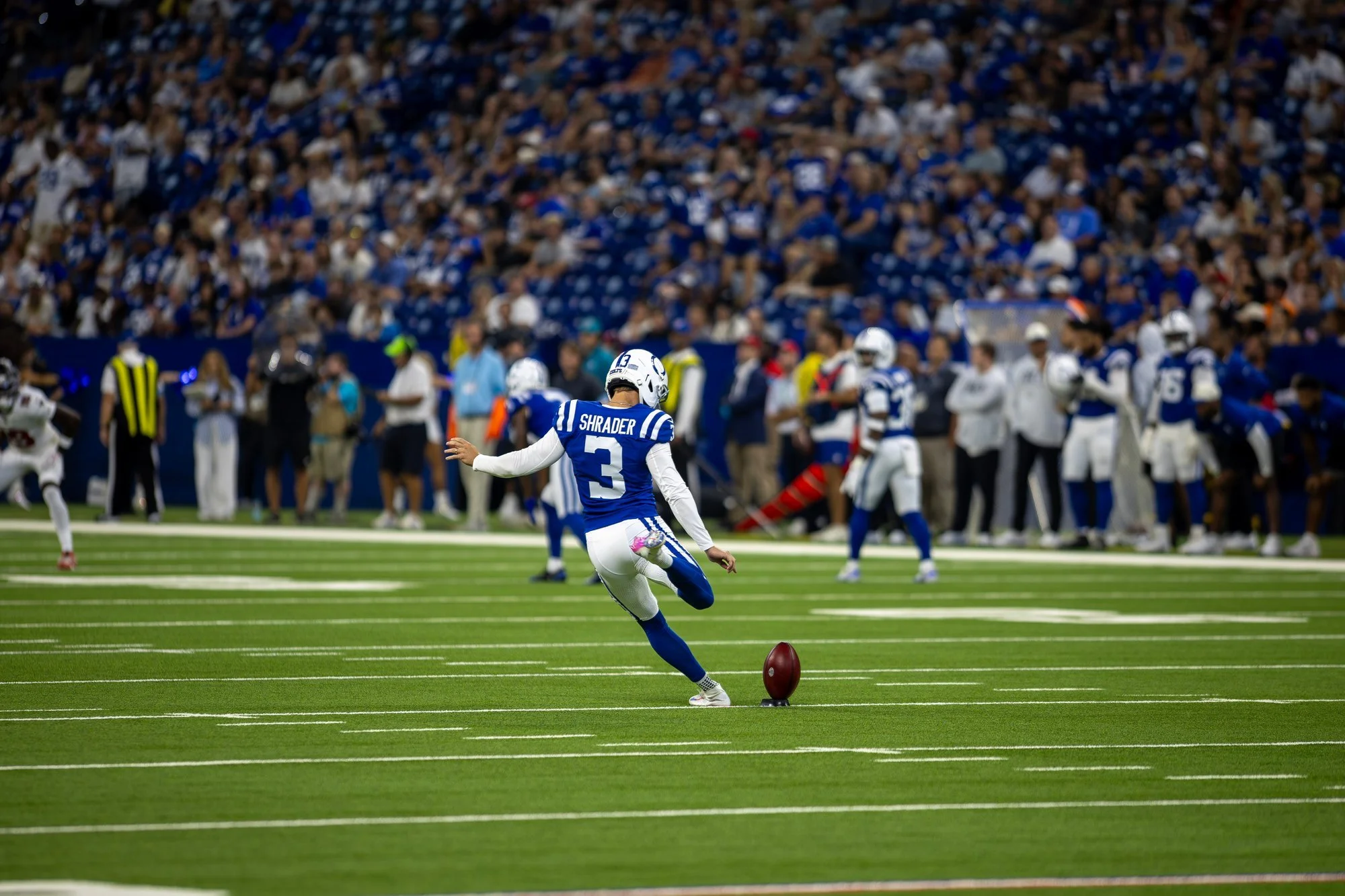 Colts kicker striking the ball on a kickoff in front of a full stadium crowd.