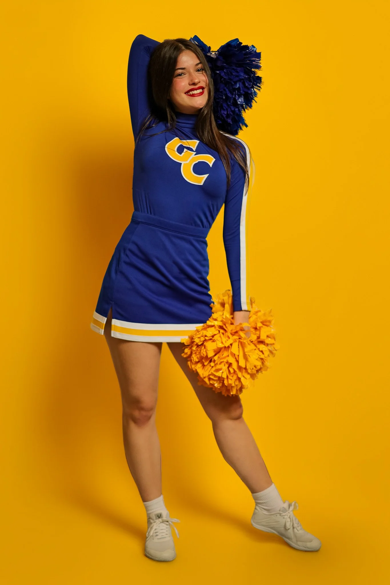 Cheerleader in blue GC uniform with pom-poms, studio portrait
