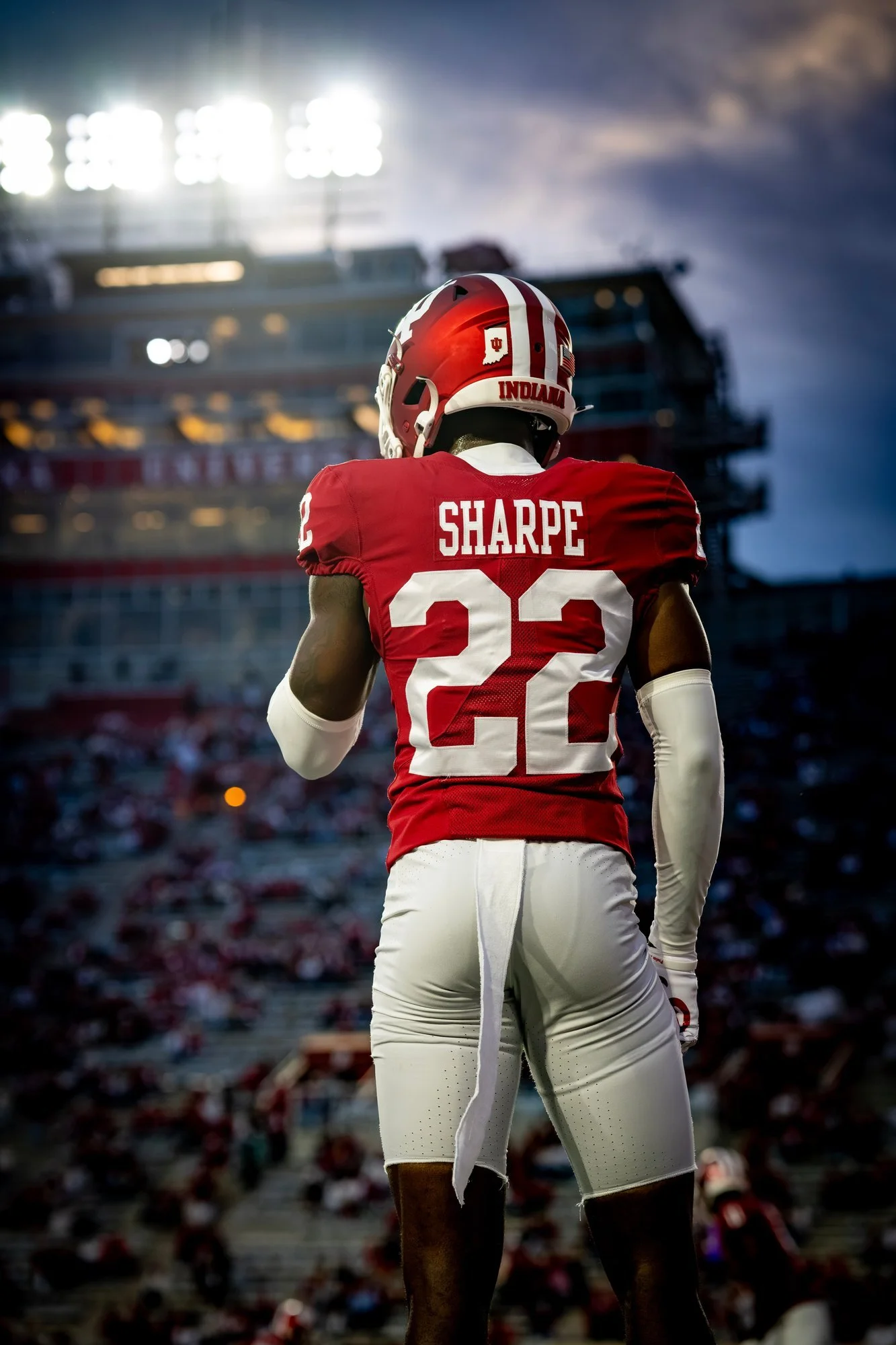 Indiana player in crimson, seen from behind, standing on the field under bright stadium lights.