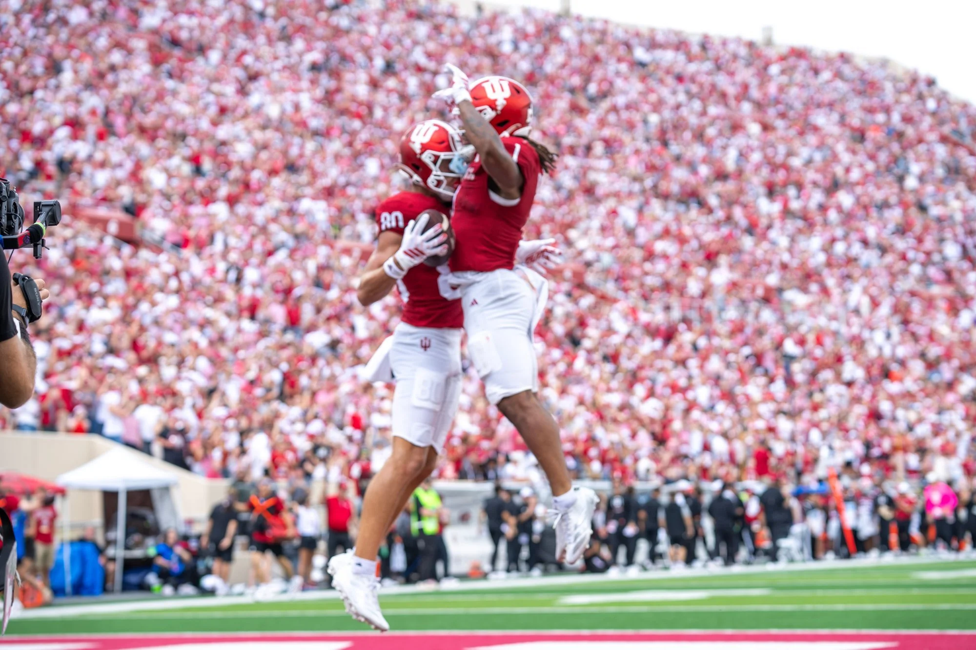 Two Indiana players leaping together in celebration in front of a packed crowd.