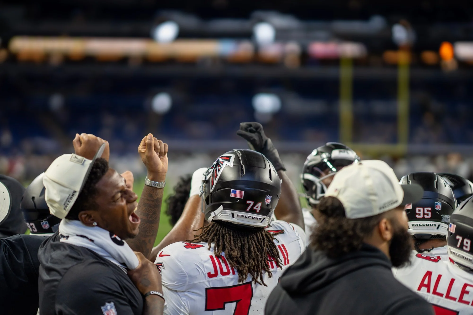 Falcons players and staff celebrating with raised fists on the sideline.