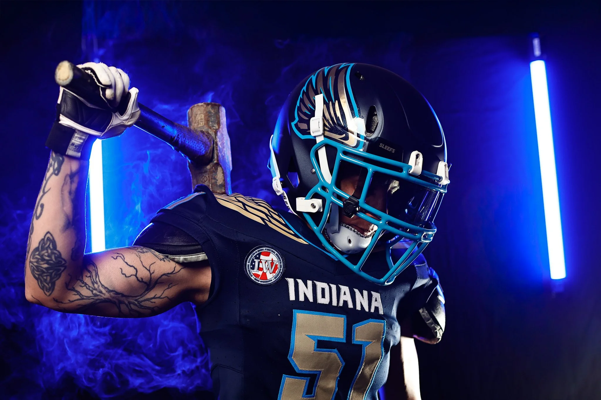 Athlete branding portrait of an Indiana Valor football player in a black helmet and jersey holding a sledgehammer over his shoulder, Indianapolis