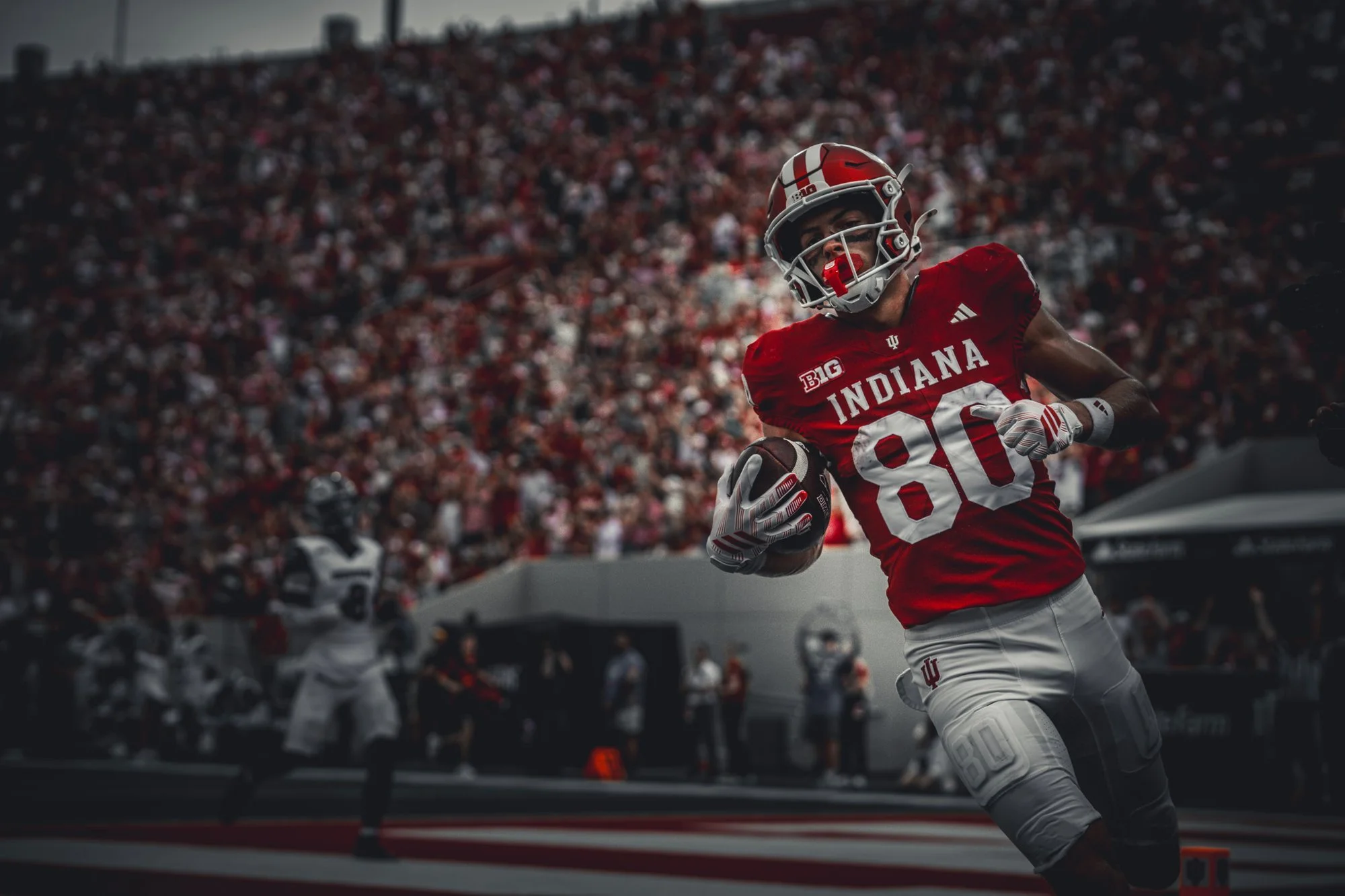 Indiana receiver in a crimson jersey running with the football against a dark background.