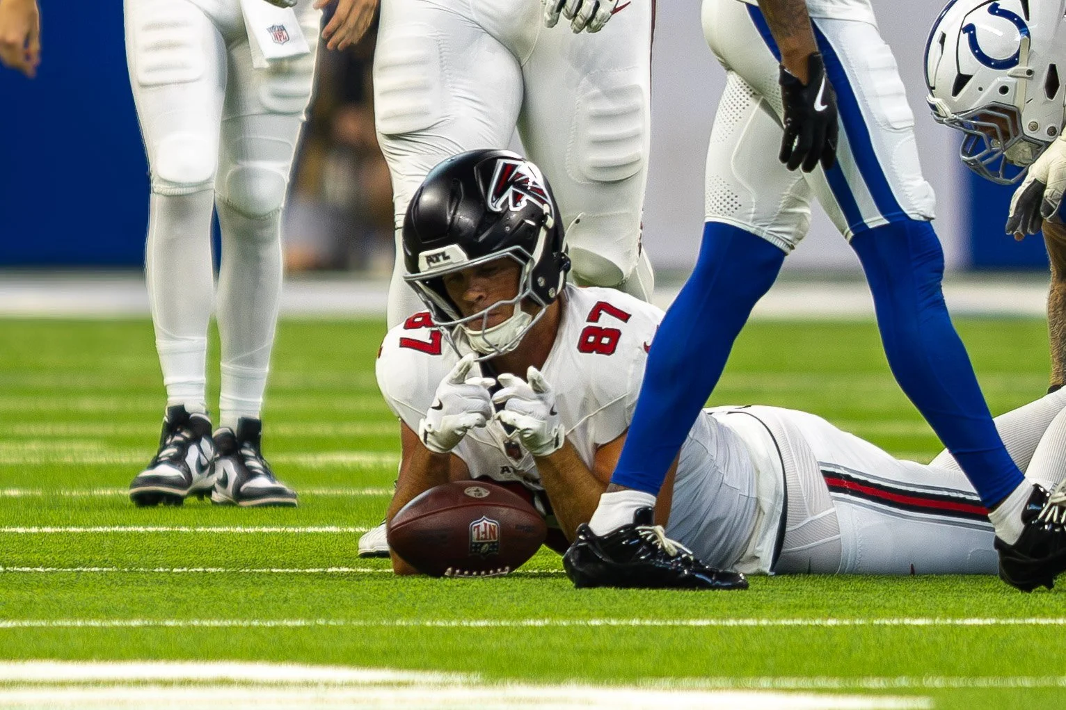 Falcons player lying on the turf after a diving catch as a Colts defender stands over him.
