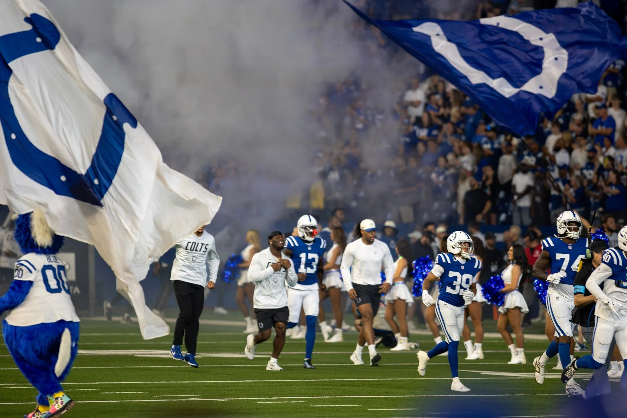 Colts players run onto the field through smoke as horseshoe flags wave during team introductions.