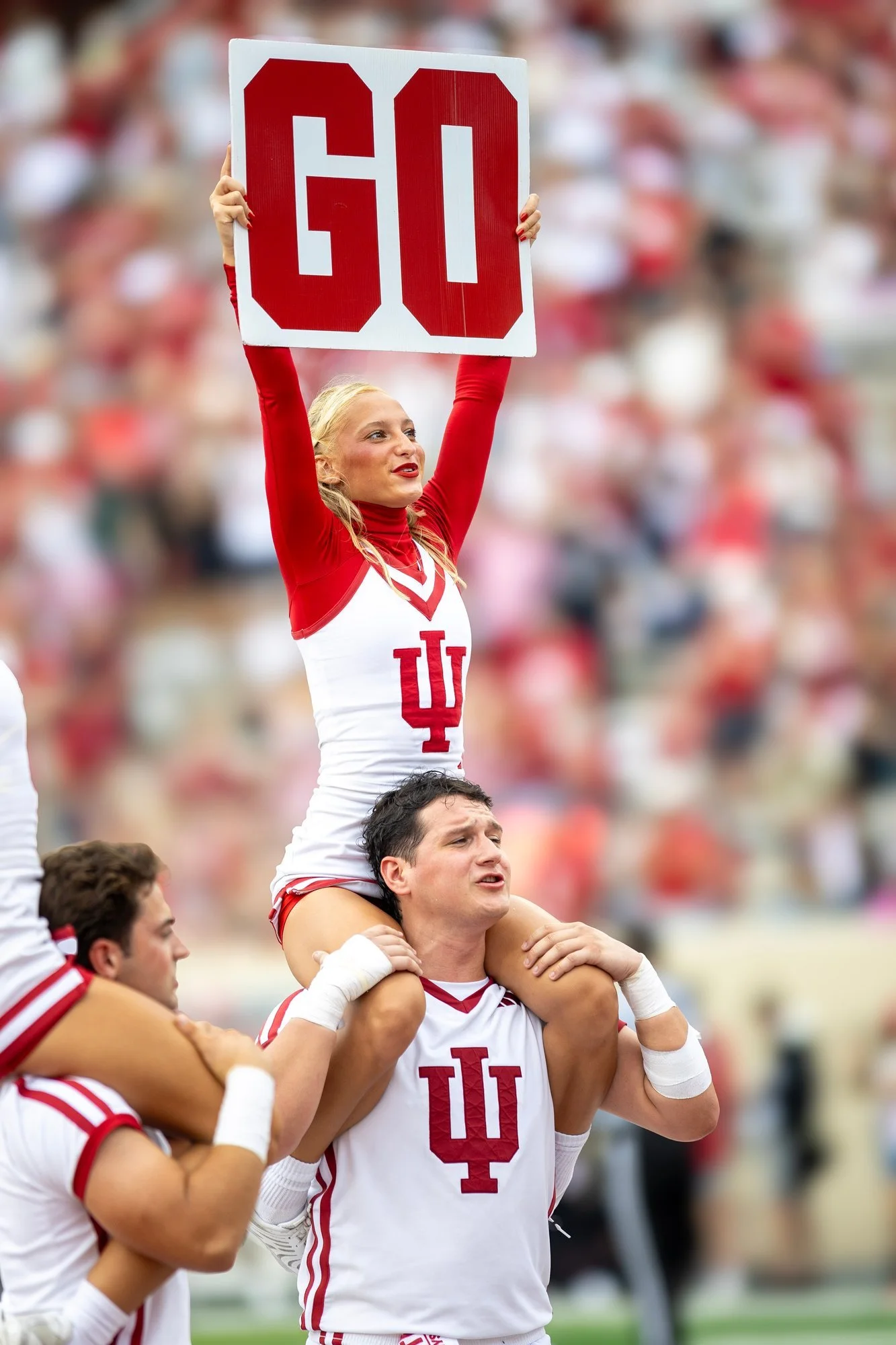Indiana cheerleader held aloft holding a GO sign.