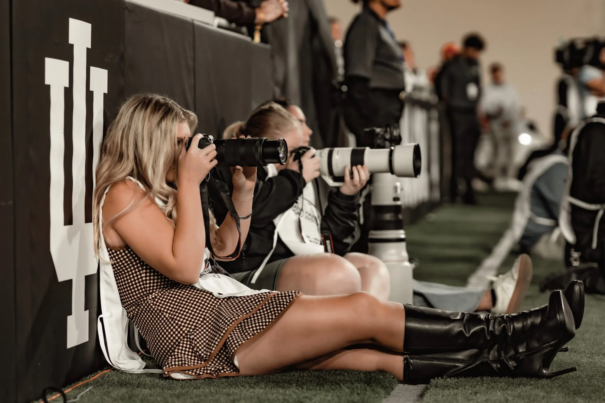 Photographer sitting against a wall shooting from the Indiana sideline.