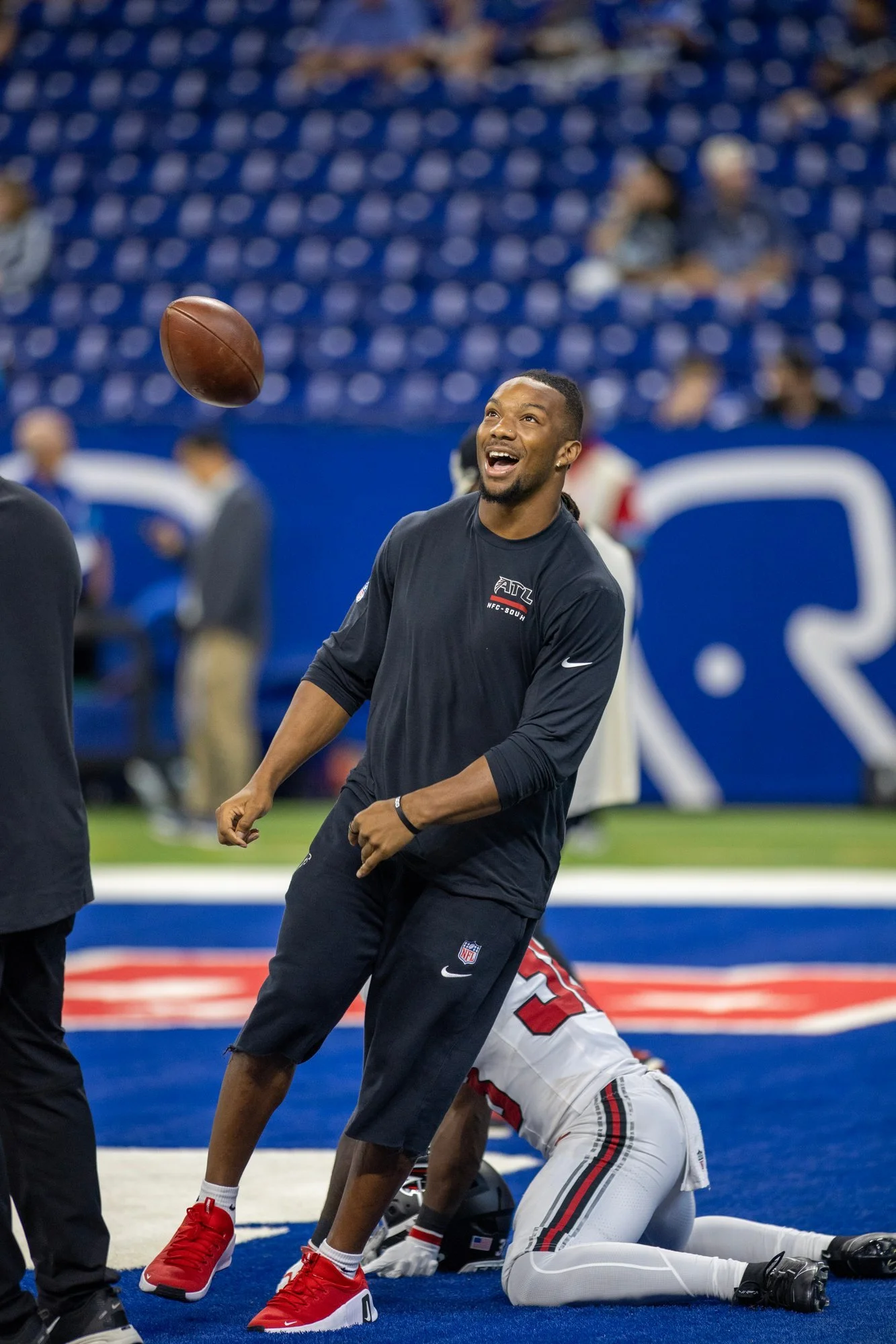 Falcons staff member smiling as a football flies through the air during pregame warmups.