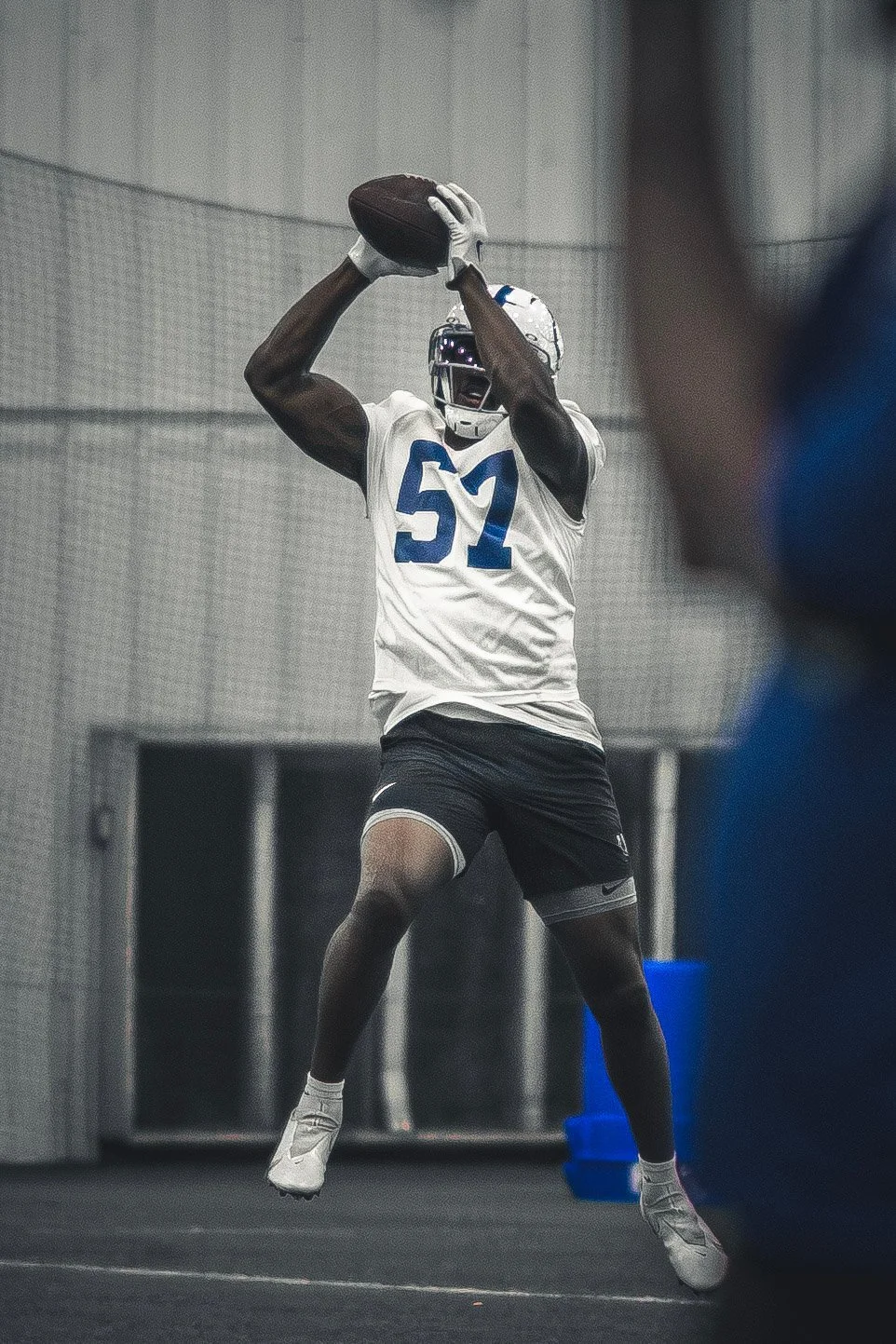 Black-and-white image of a Colts player catching a football overhead at practice.
