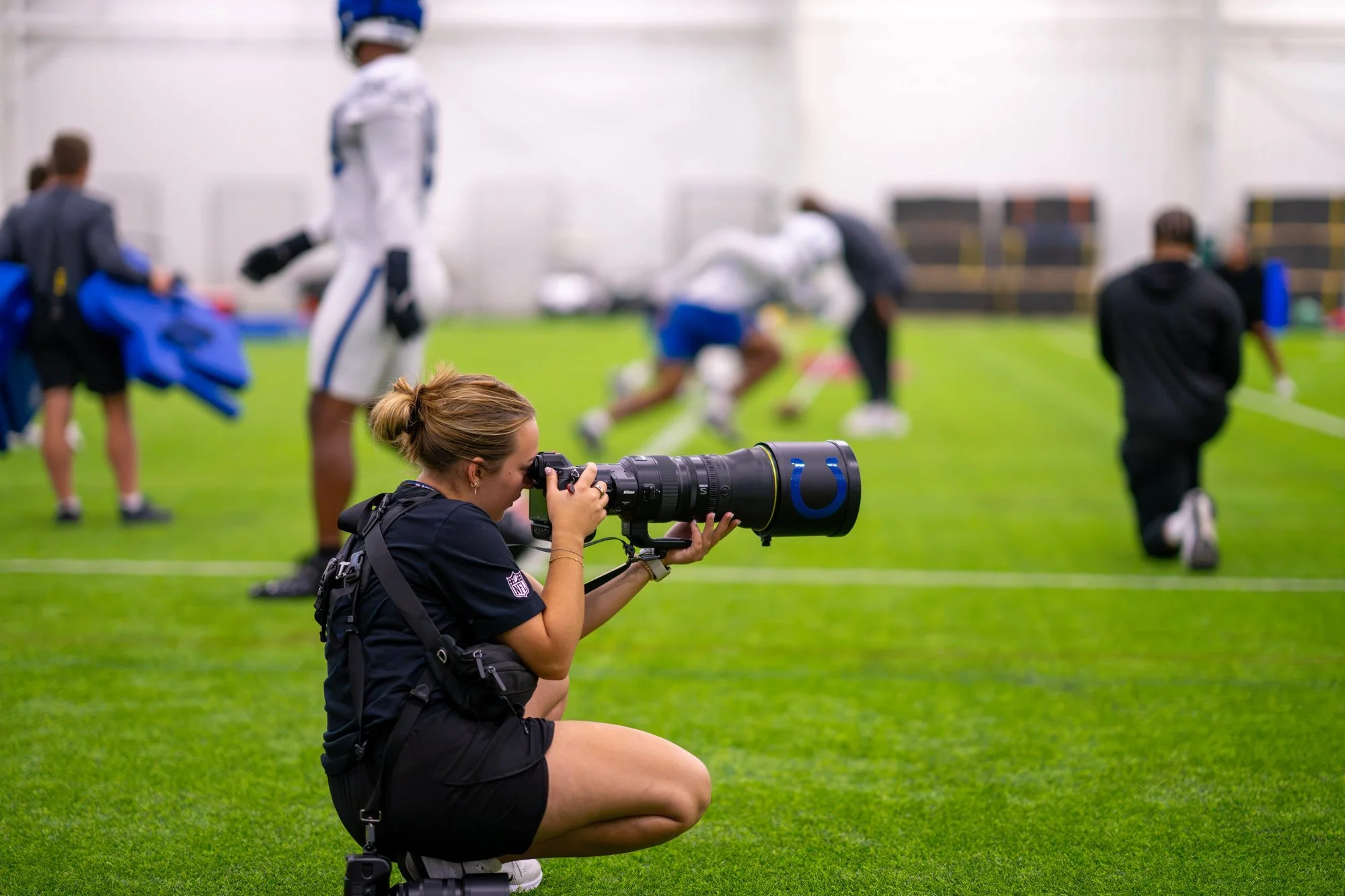 Photographer kneeling with a telephoto lens to shoot a Colts training camp drill.