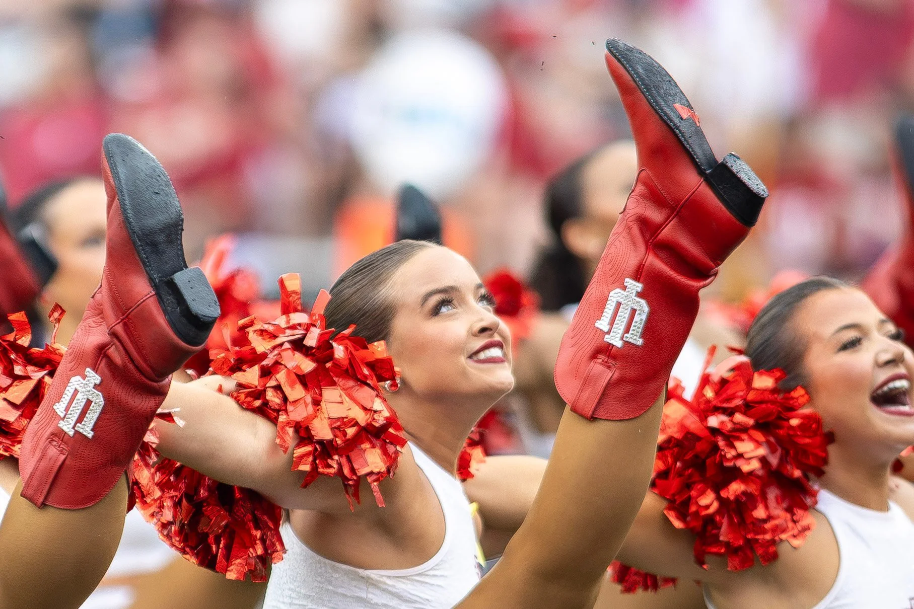 Indiana cheerleaders with red pom-poms smiling mid high kick.