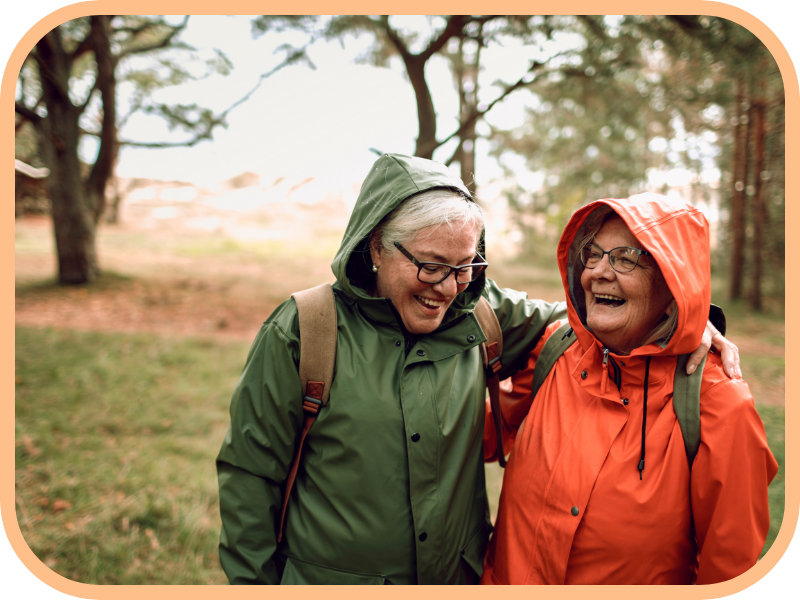 Two older women laugh together while walking outdoors in rain jackets
