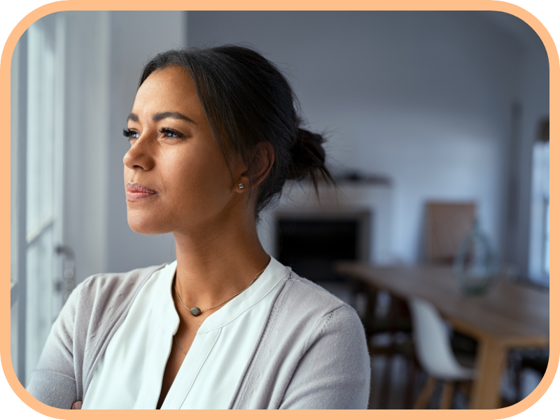 Thoughtful woman stands indoors looking out a window