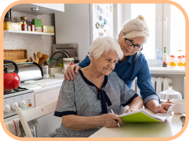Caregiver supports an older woman reviewing information at a kitchen table