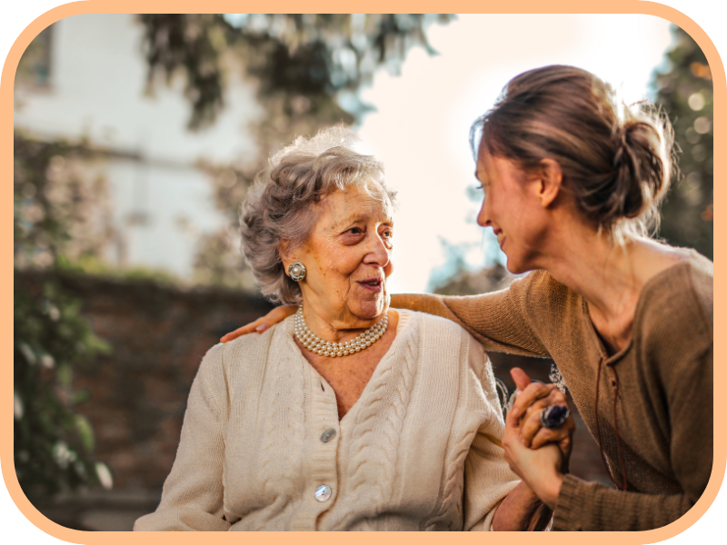 Caregiver holds hands and talks with an older woman outdoors