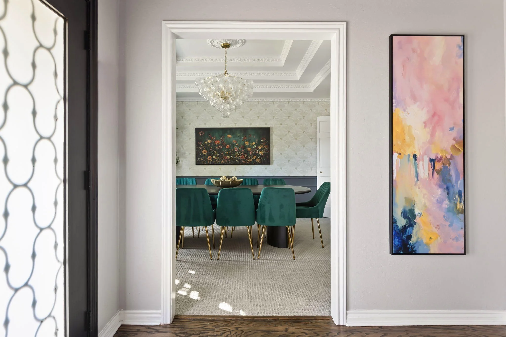 Dining room in a luxury short-term rental designed by Kelsey Brown Interiors. Includes velvet, emerald green dining chairs, a large wooden dining table, globe chandelier and abstract artwork. 