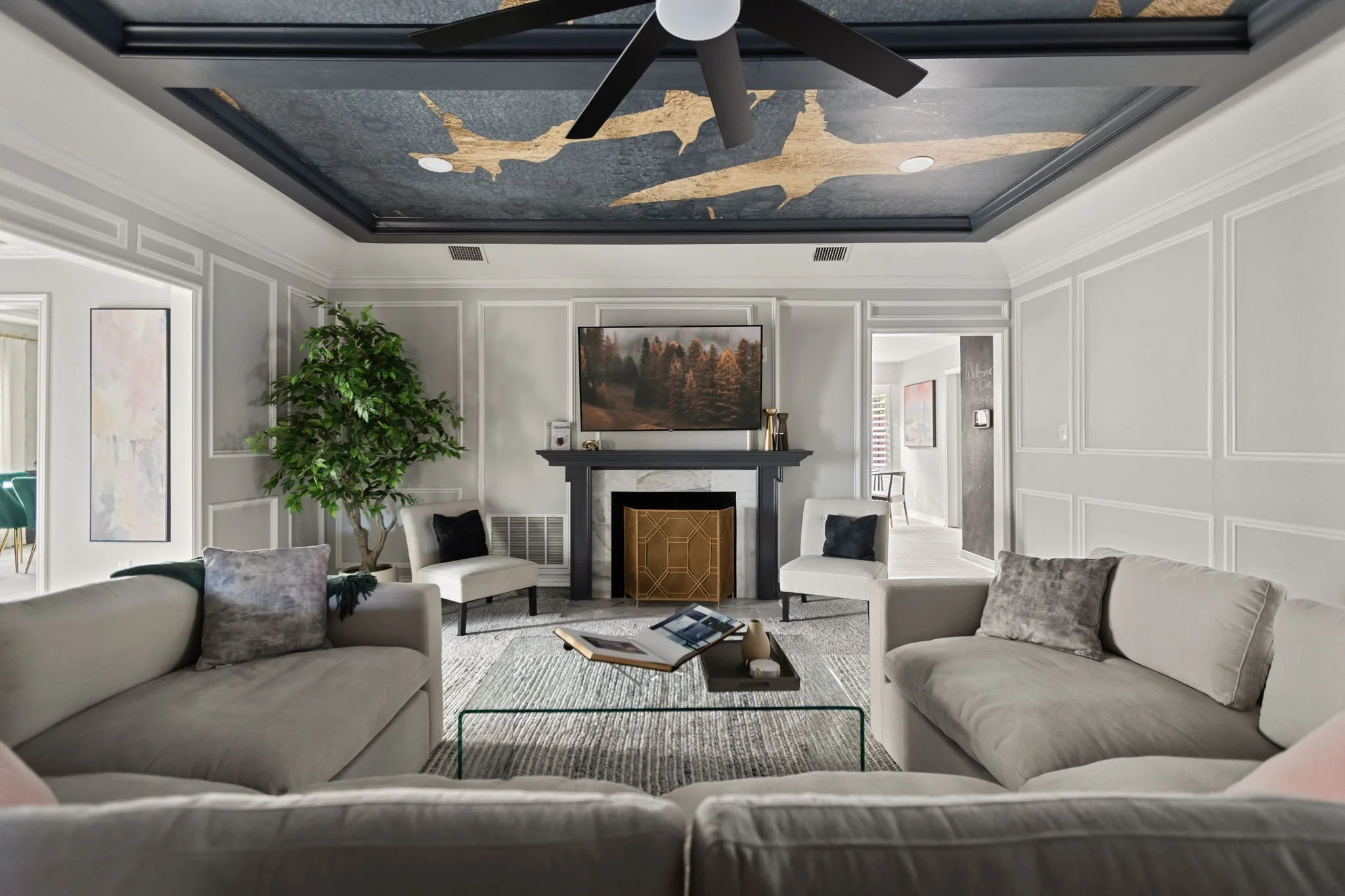 Living room in a luxury, short-term rental in the Dallas area. Showcases a golden bird mural on the ceiling. There is a large sectional and acrylic coffee table. Designed by Kelsey Brown Interiors.