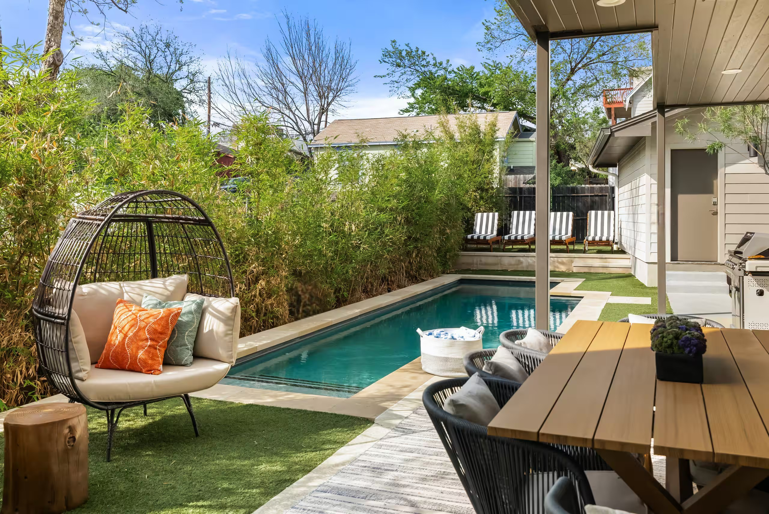 Outdoor space designed by Kelsey Brown Interiors. Features a modern outdoor dining table and chairs next to a pool and turf with eggs chairs and striped lounge chairs in Austin, Texas.