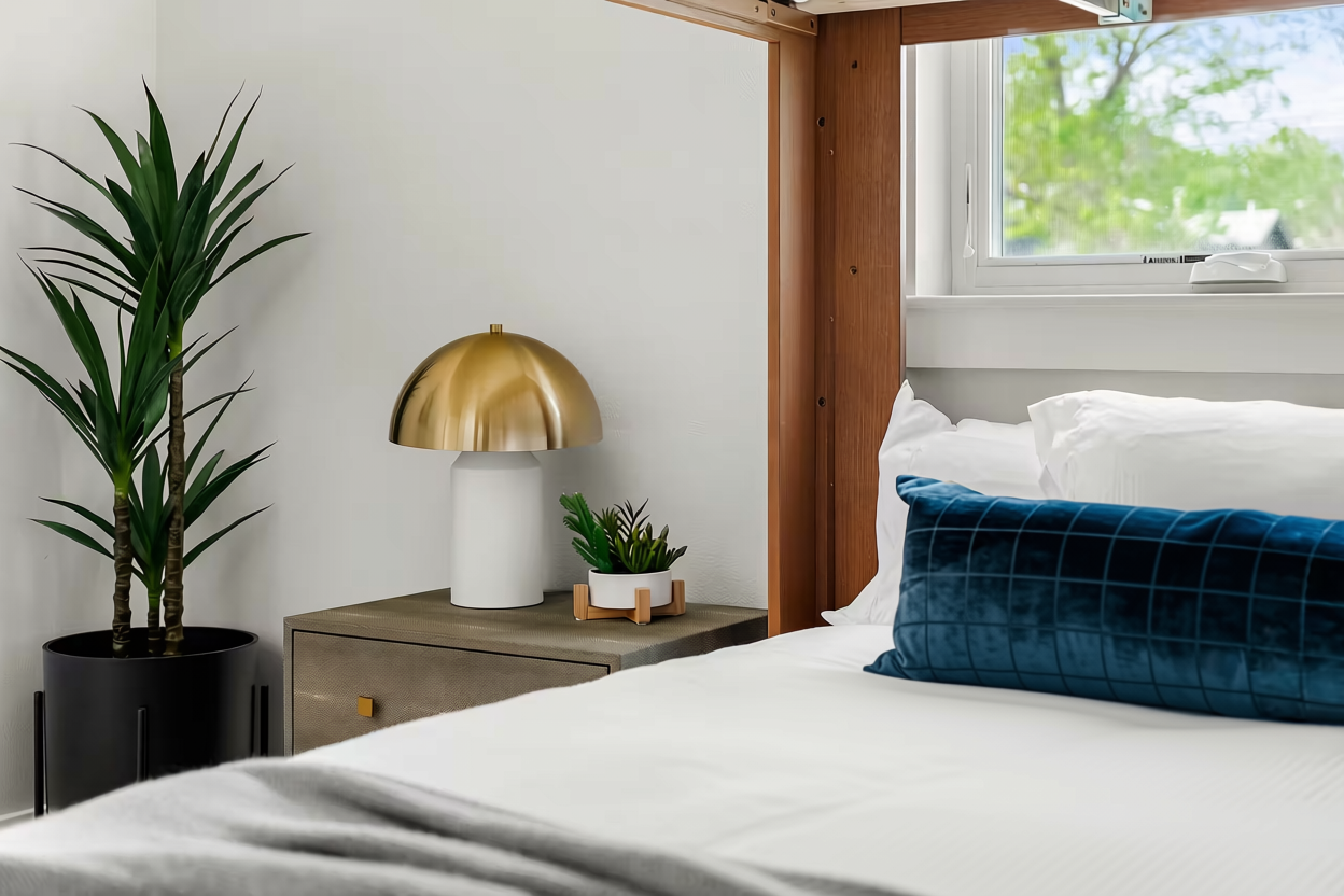 Vignette of bunk beds in an Austin short-term rental designed by Kelsey Brown Interiors. Features a velvet blue lumbar pillow, gold and brass lamp, and house plants.