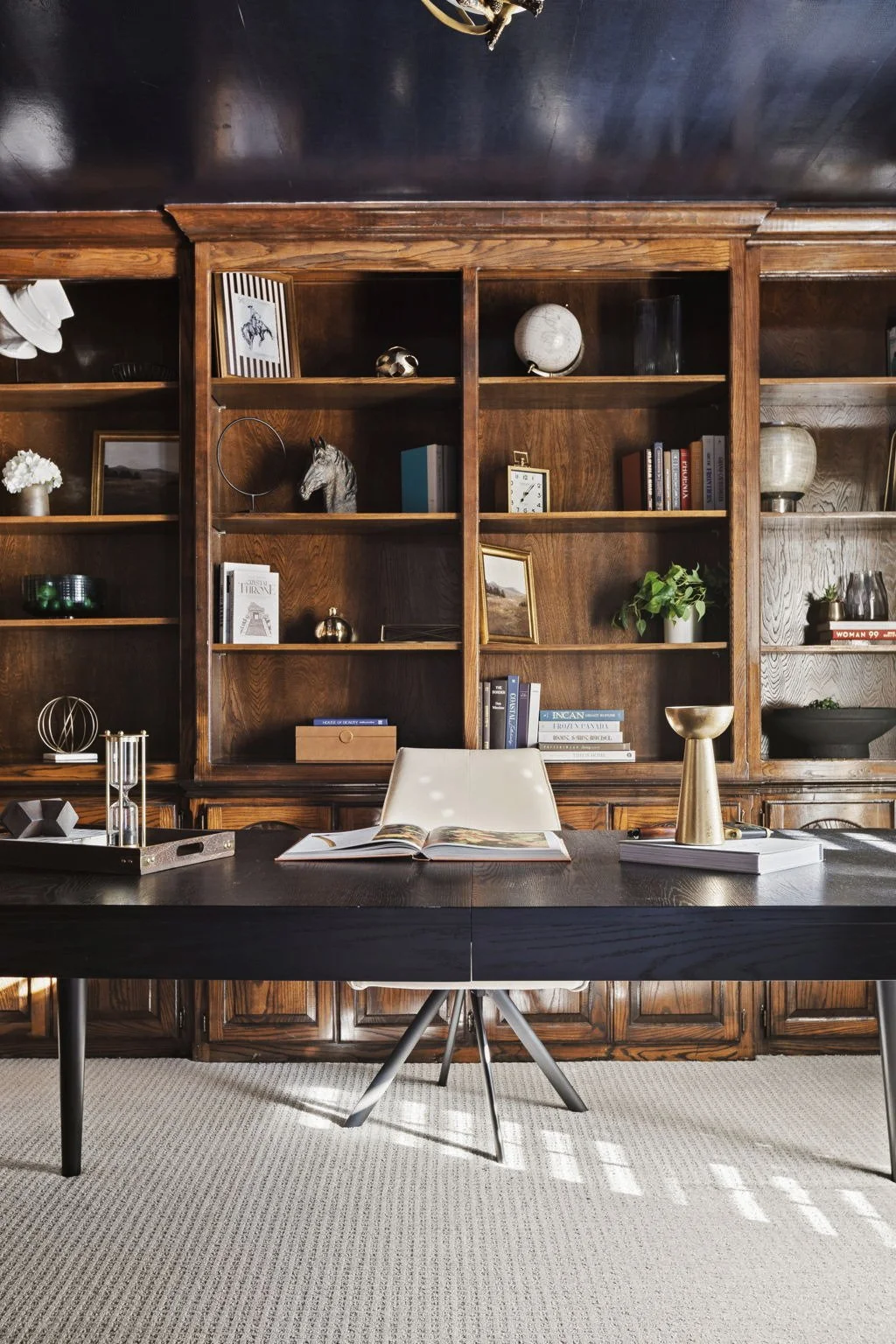 Short-term rental office in the Dallas area designed by Kelsey Brown Interiors. Showcases a shiny, snake skin wallpaper on the ceiling. behind the black desk, there's a mahogany bookshelf.