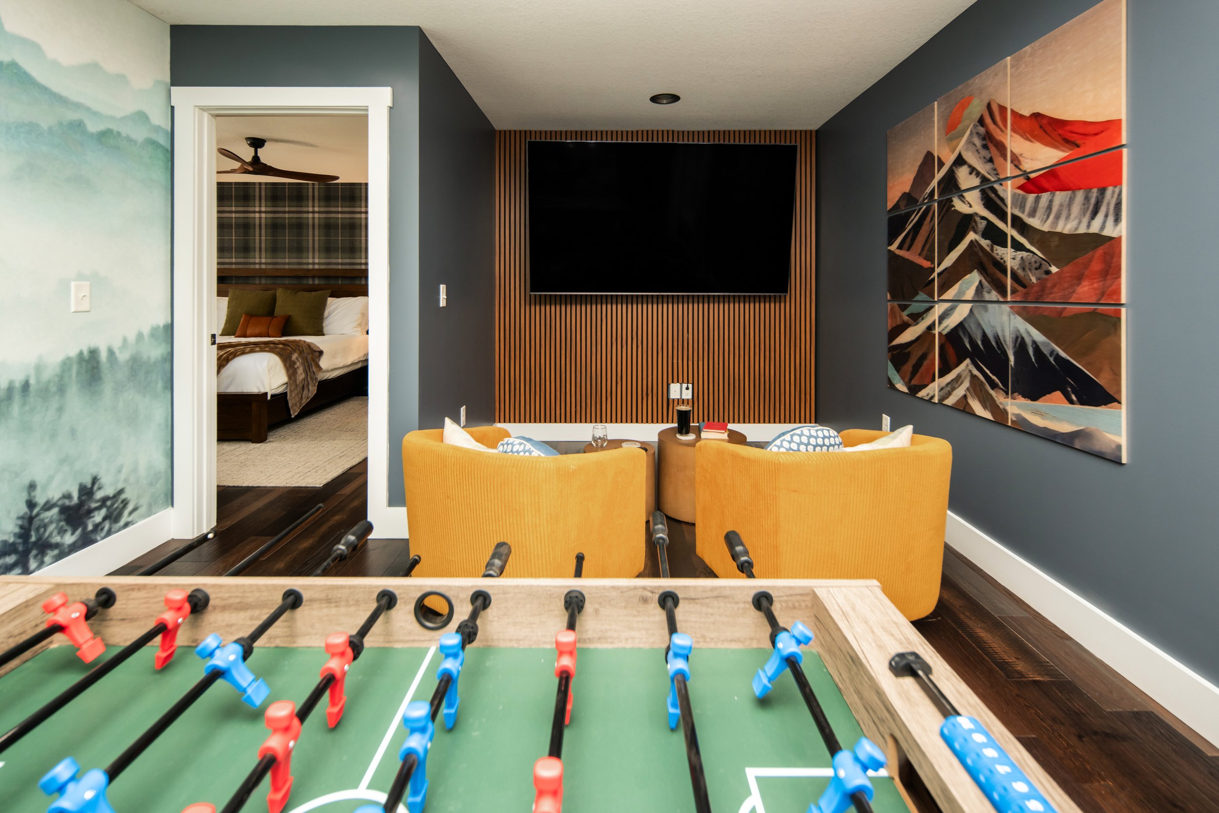 Moody blue game room with a foosball table, seating area, and forest mural in Asheville, North Carolina designed by Kelsey Brown Interiors.