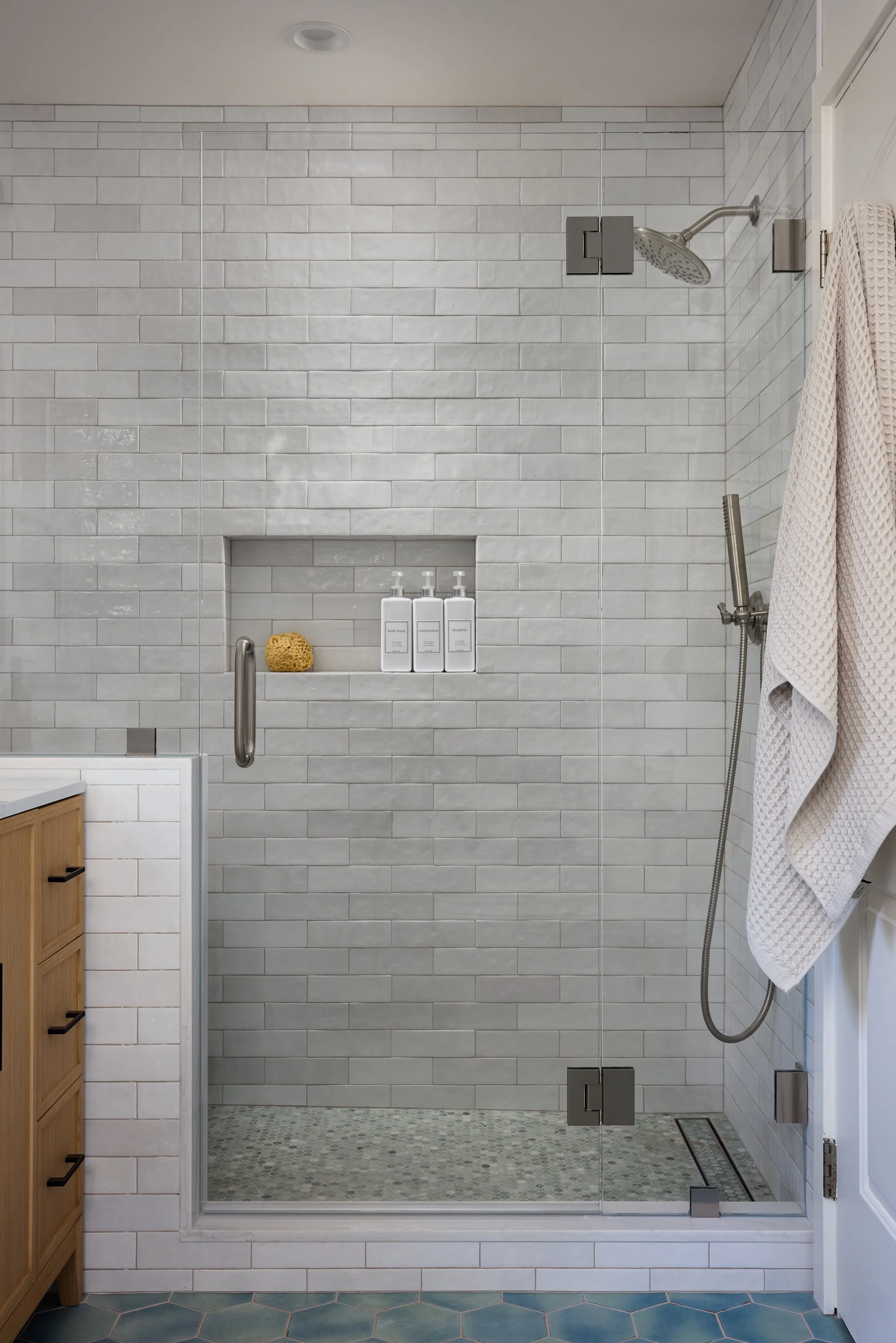 Transitional coastal primary shower designed by Kelsey Brown Interiors. Features brushed nickel fixtures, green marble penny tile, and textured subway tile. Design for an Aptos, California bathroom renovation.
