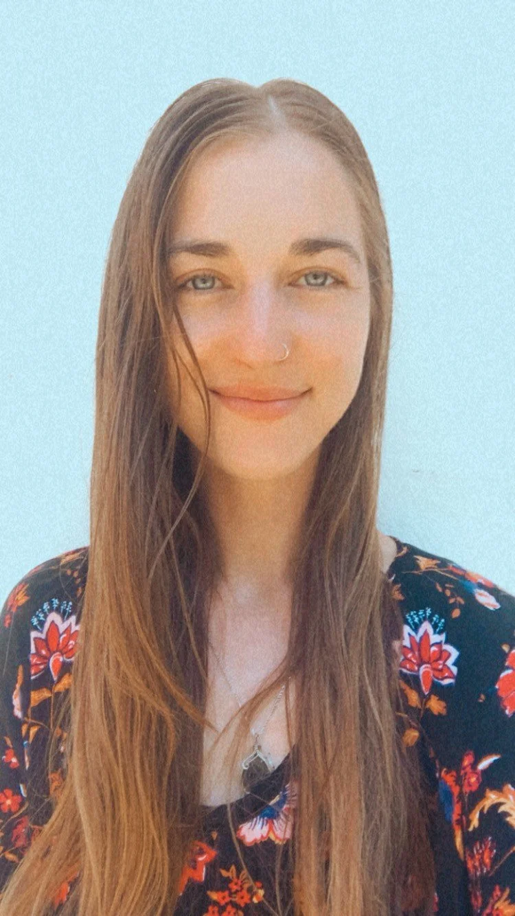 Person with long hair, wearing a floral top, smiling.