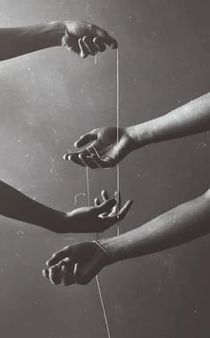 Three hands intertwined with strings in a monochrome setting.