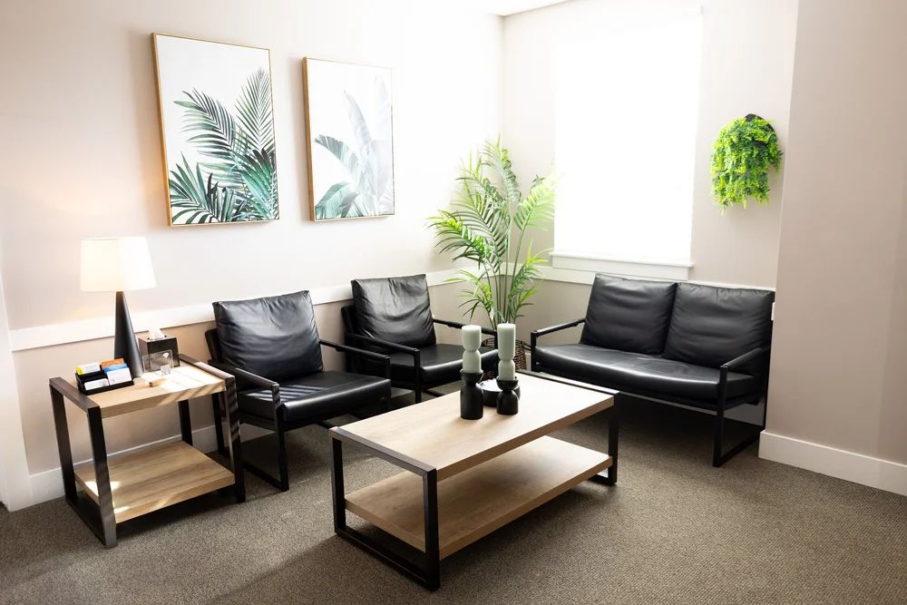 The waiting room at Healing Hearts Counseling in Murray, Utah, with black leather seating, a wood coffee table and palm leaf artwork.