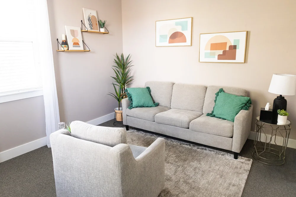 The waiting area at Healing Hearts Counseling in Murray, Utah, with a light sofa, an armchair, artwork, a plant and a lamp.