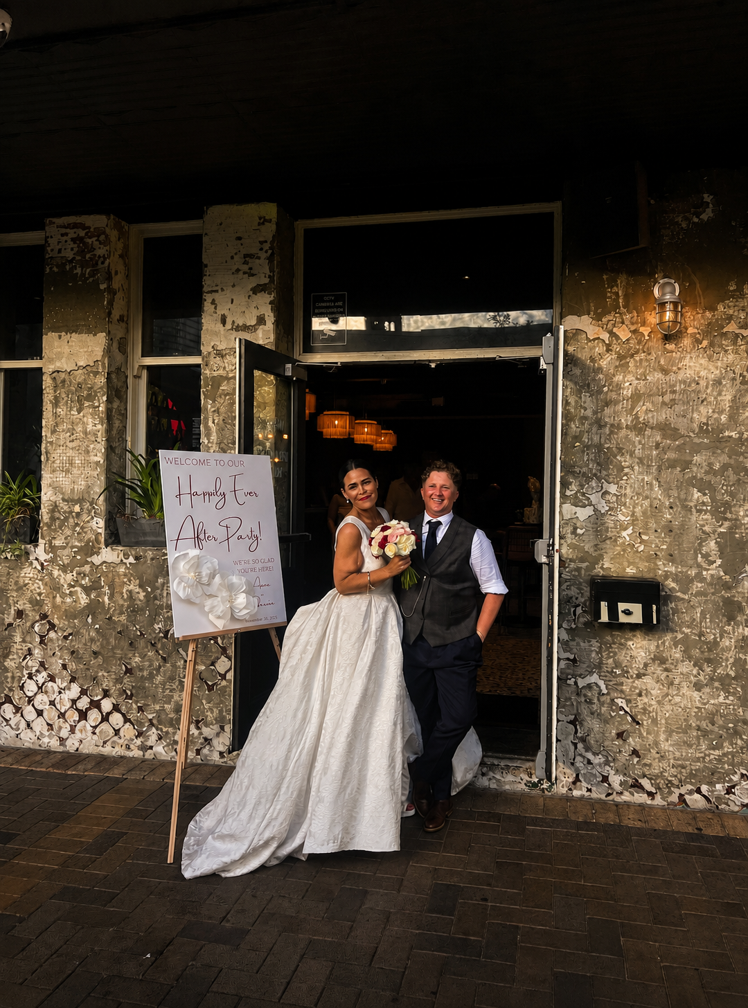 Newlyweds posing beside their wedding welcome sign outside their reception venue in Brisbane, photographed by Socials Only.