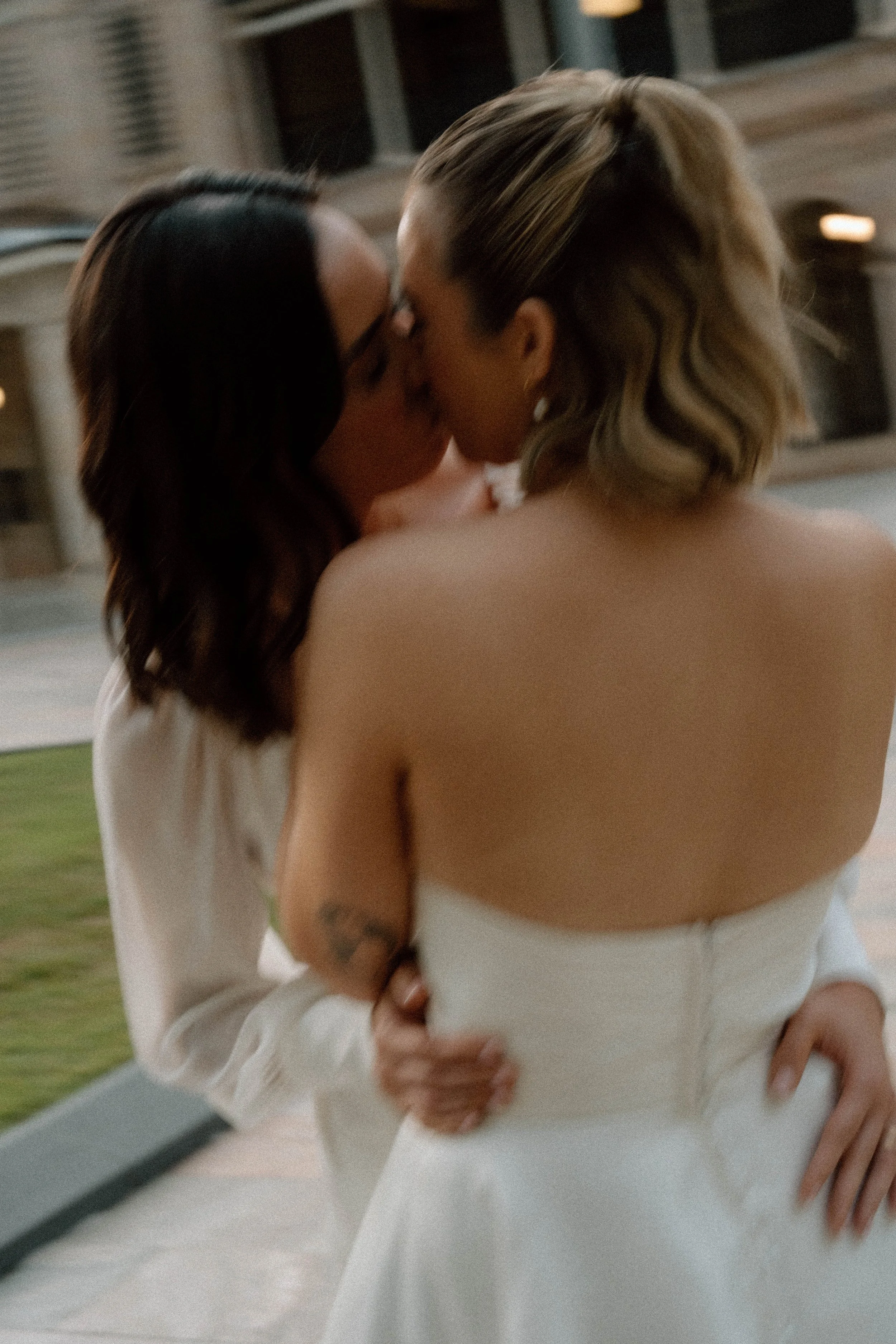 Two brides celebrating their wedding ceremony with a kiss beneath a floral arch at an outdoor Queensland wedding venue.