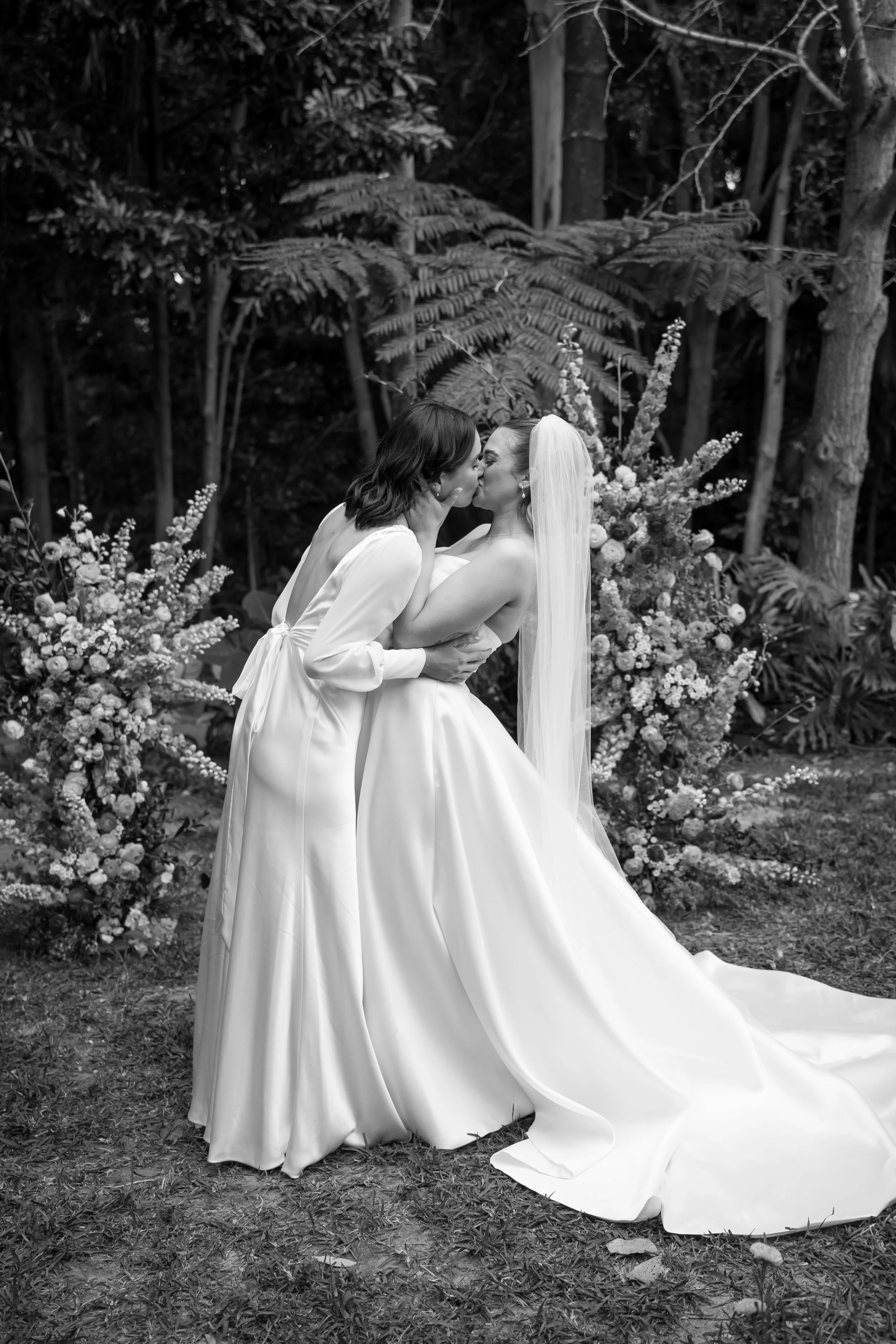 Two brides sharing a kiss after their wedding ceremony, surrounded by floral arrangements, captured by Brisbane wedding content creator Socials Only.