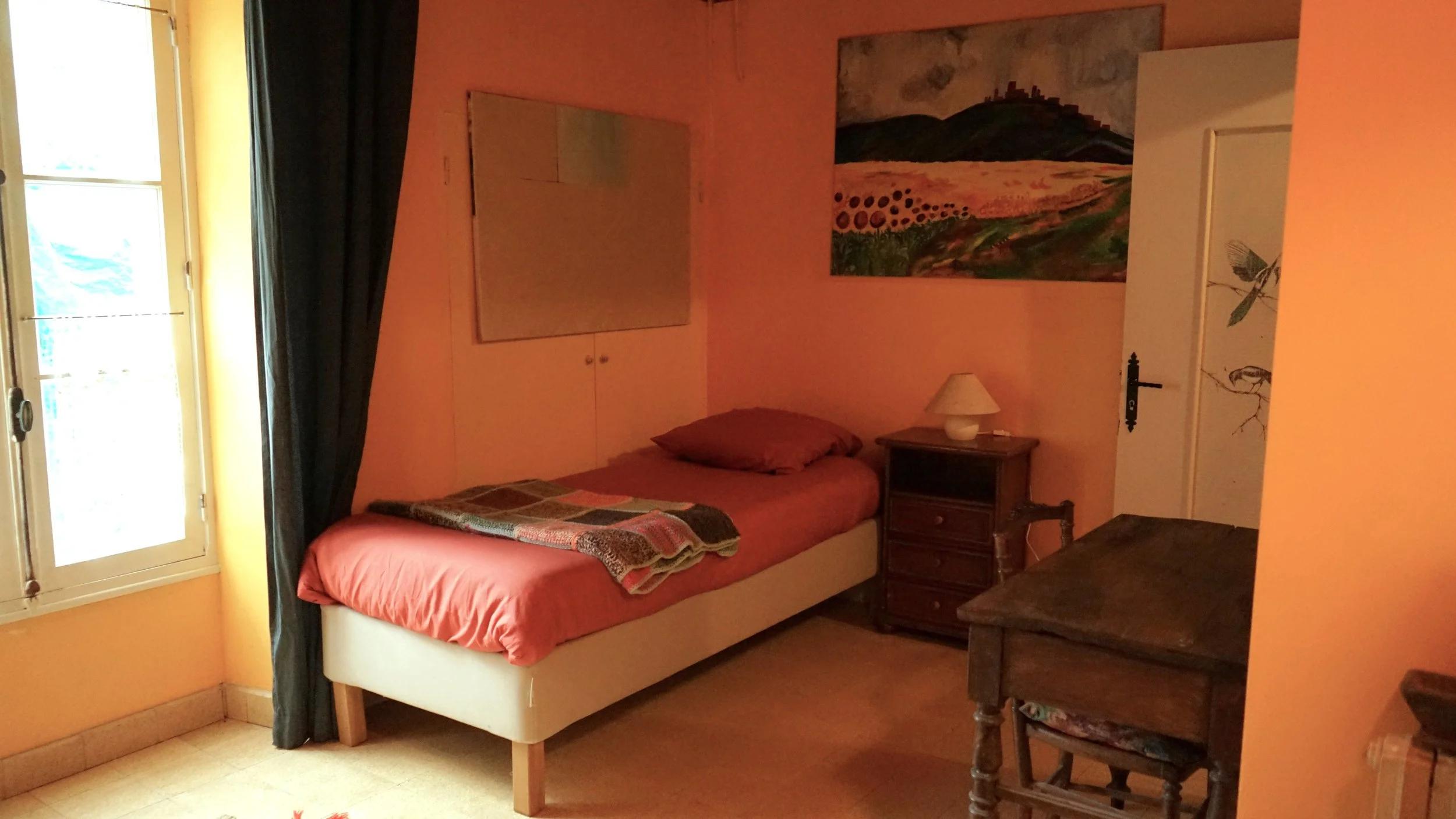 A bedroom with a bed, blue curtains, a window, a colorful rug, and a painting of horses on the wall.
