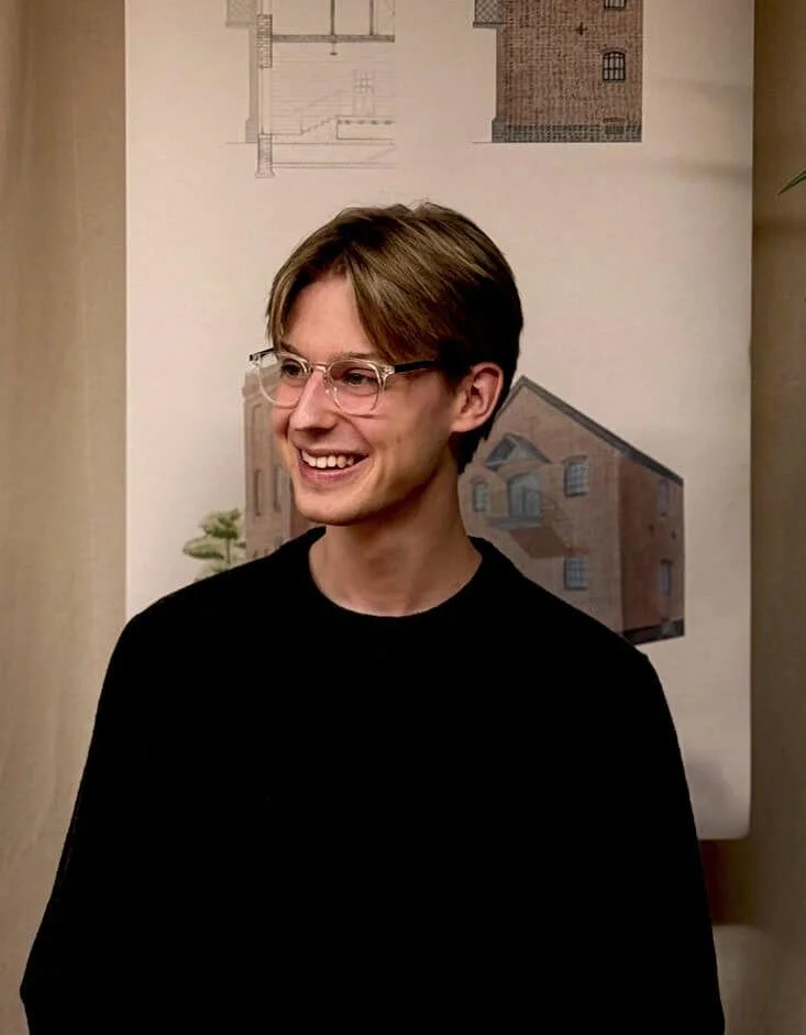 24/Three Beck, Architectural Assistant, working at his desk with a smile