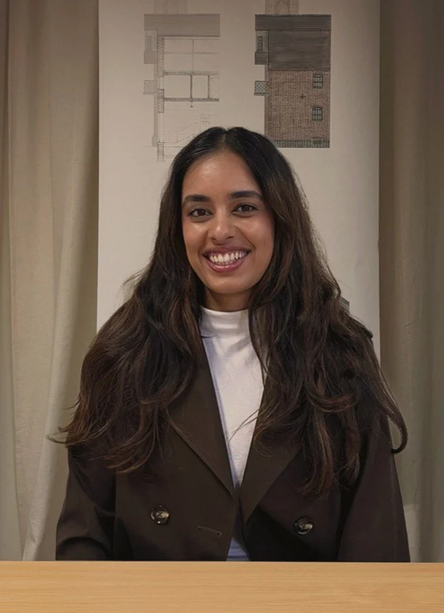 24/three priya wearing a brown jacket and smiling directly into camera