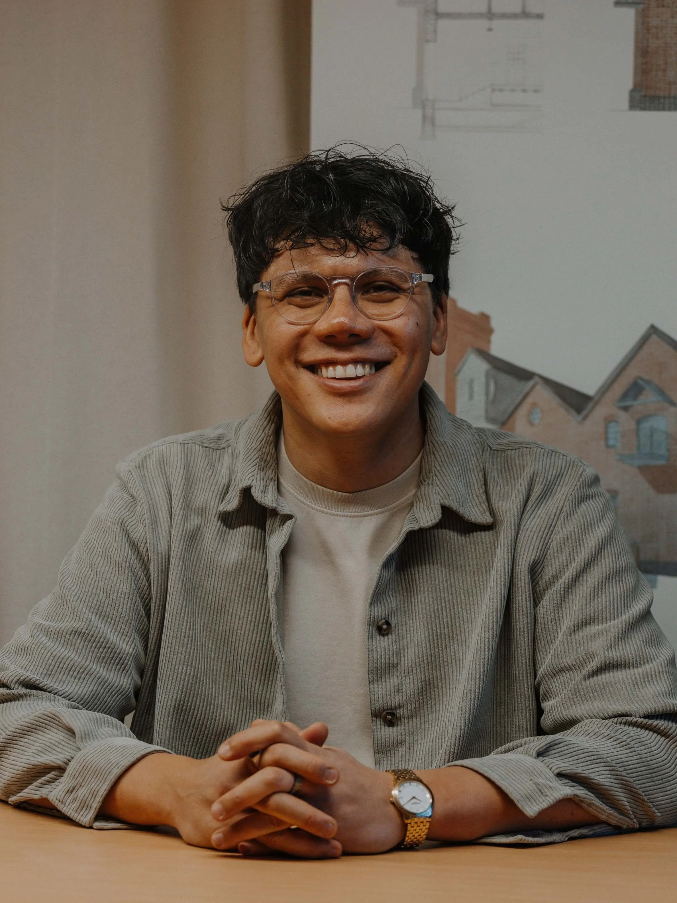 Mark, team member at 24/Three architecture studio, smiling while seated at a desk with architectural plans