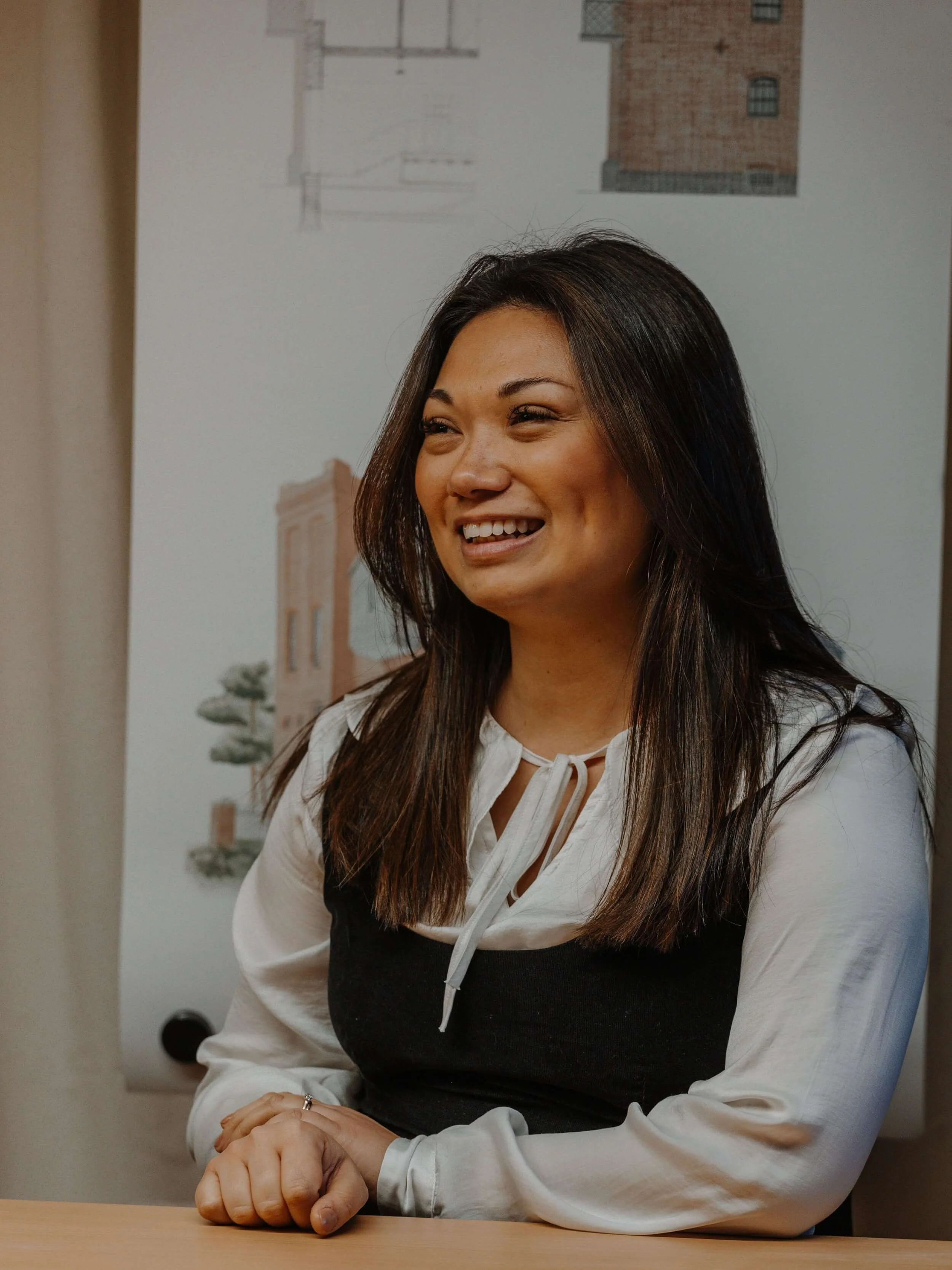 Leah, architectural designer at 24/Three, smiling at a table with architectural drawings in the background