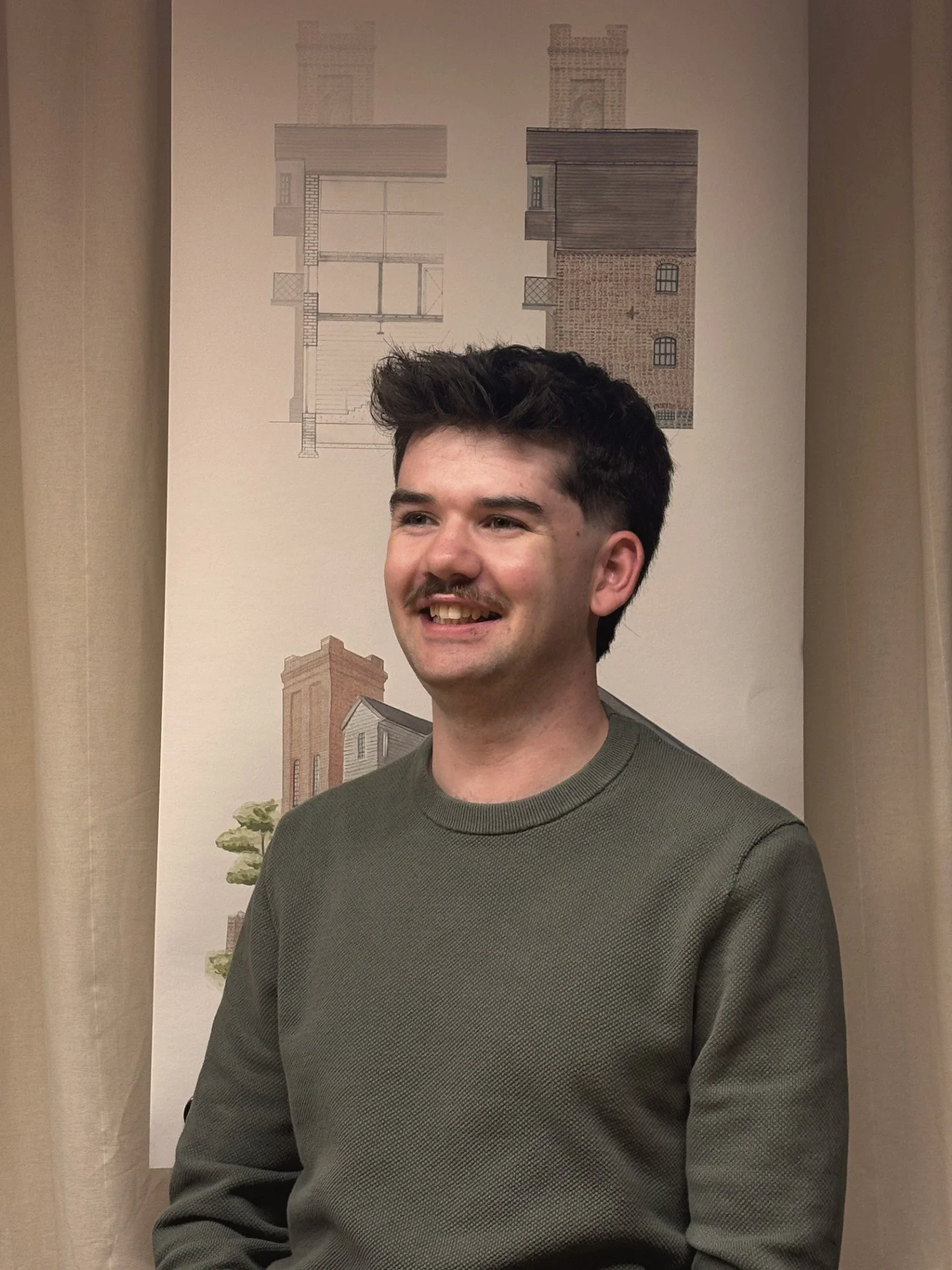 Nathan from the 24/Three team in a green jumper posing in front of a watercolour sketch